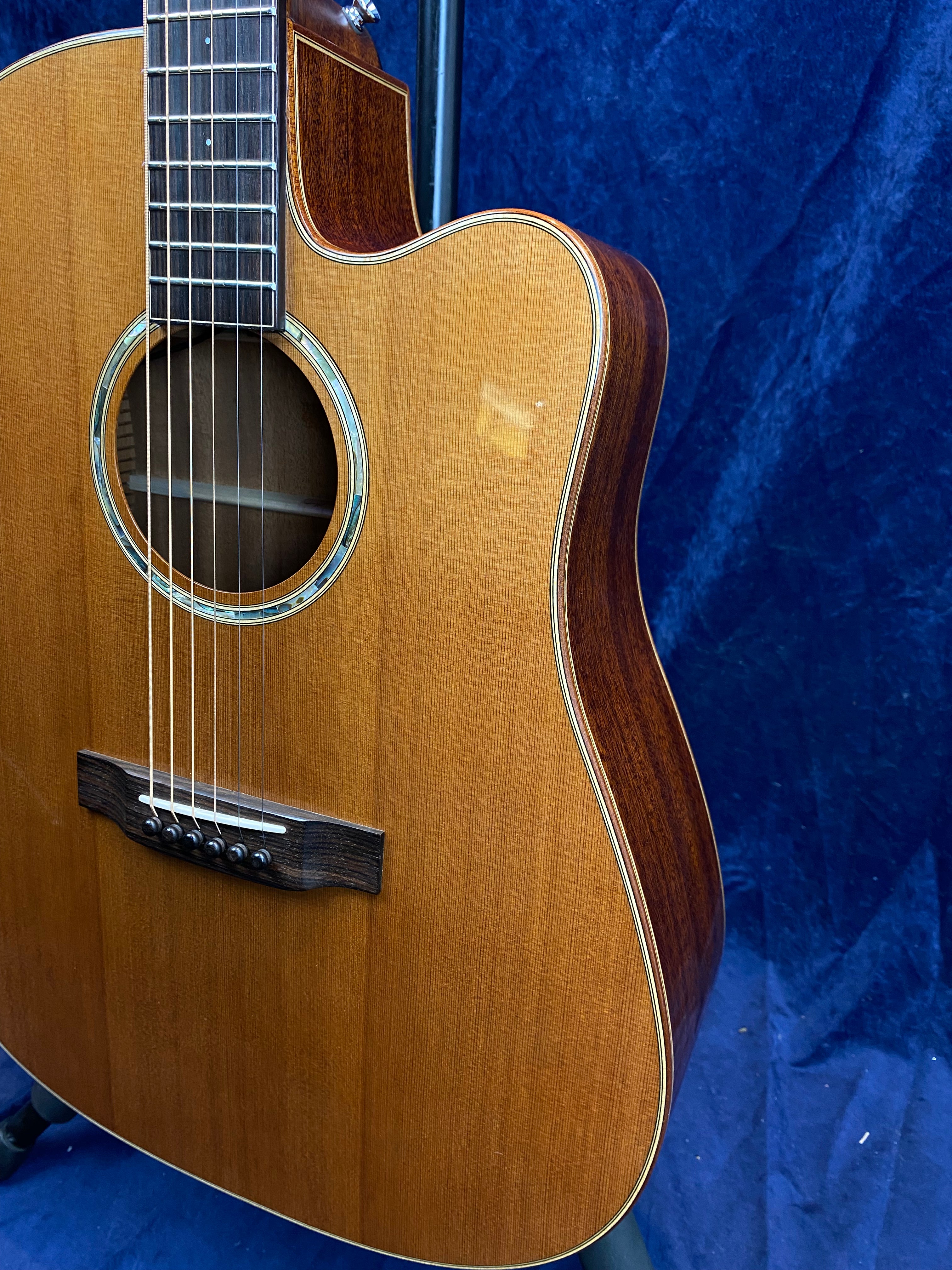 Glossy wooden acoustic guitar with a cutaway design, six strings, circular sound hole, and decorative ring around the opening.