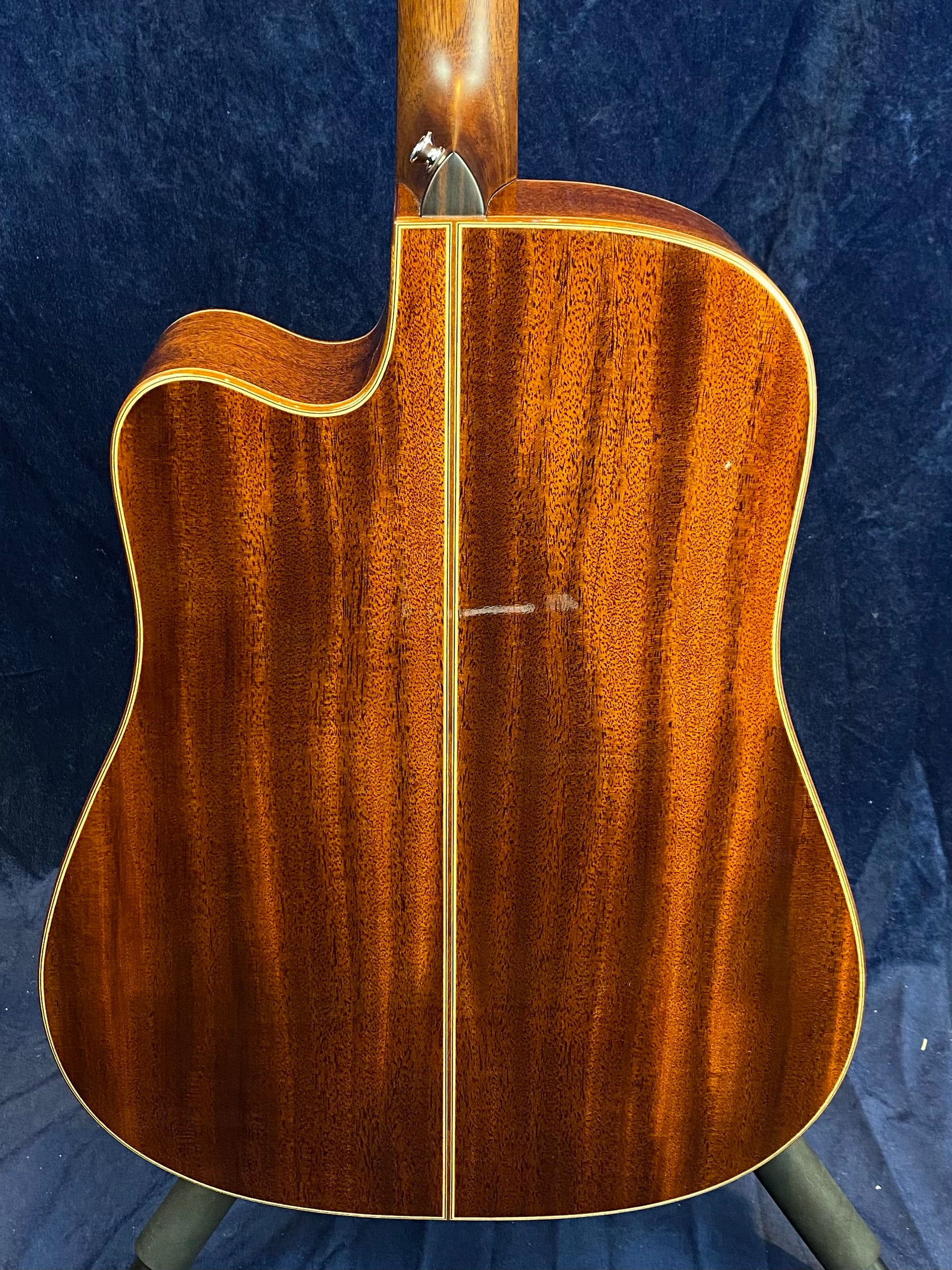 Acoustic guitar back view showing glossy, reddish-brown wood with a vertical center seam and light wood binding along the edges.