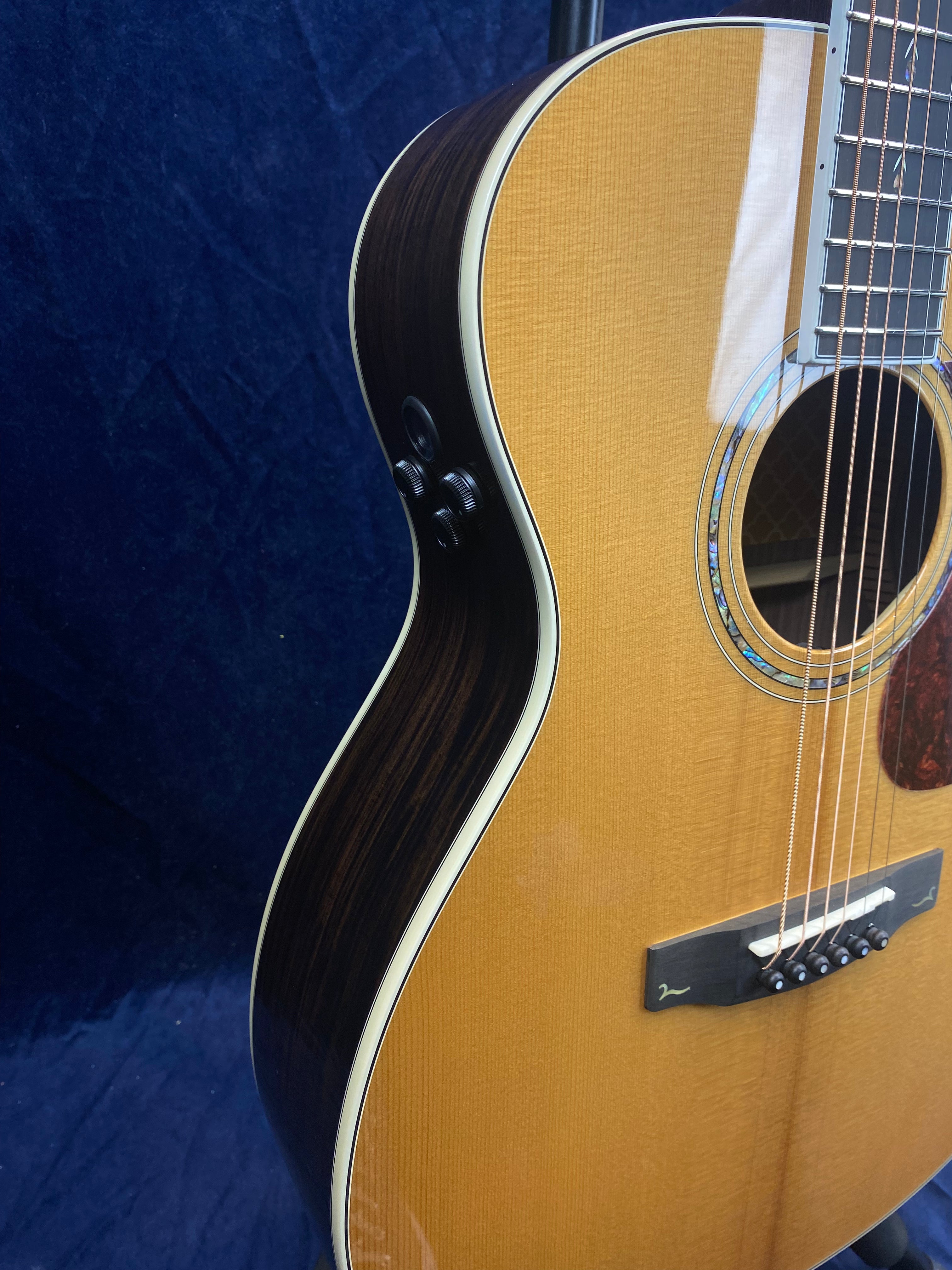 Glossy light wood acoustic guitar with dark sides, white trim, two black control knobs on the upper side, and six strings visible near the soundhole.