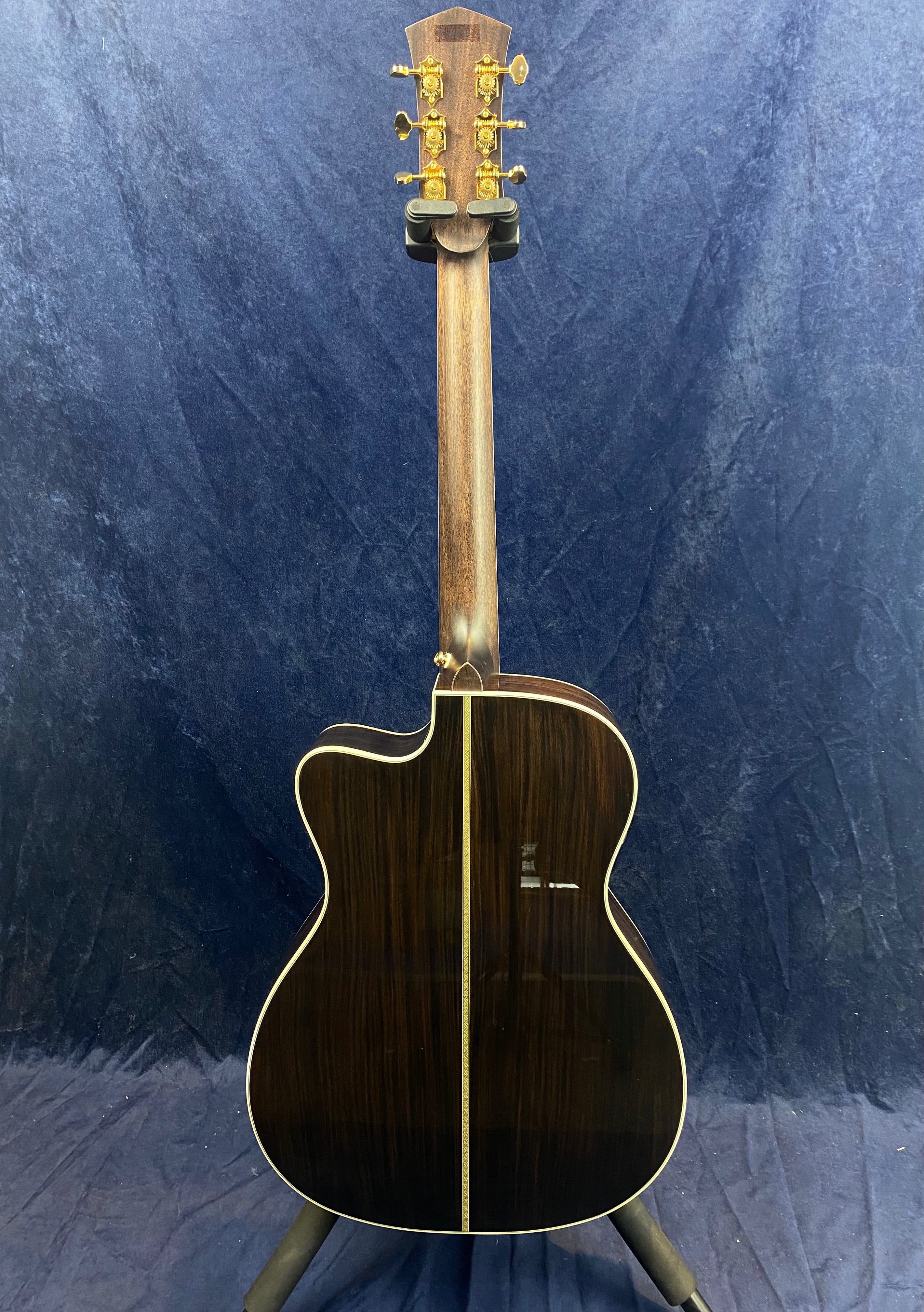 Acoustic guitar shown from the back, with dark wood, light binding along the edges, and gold tuning pegs on the headstock.
