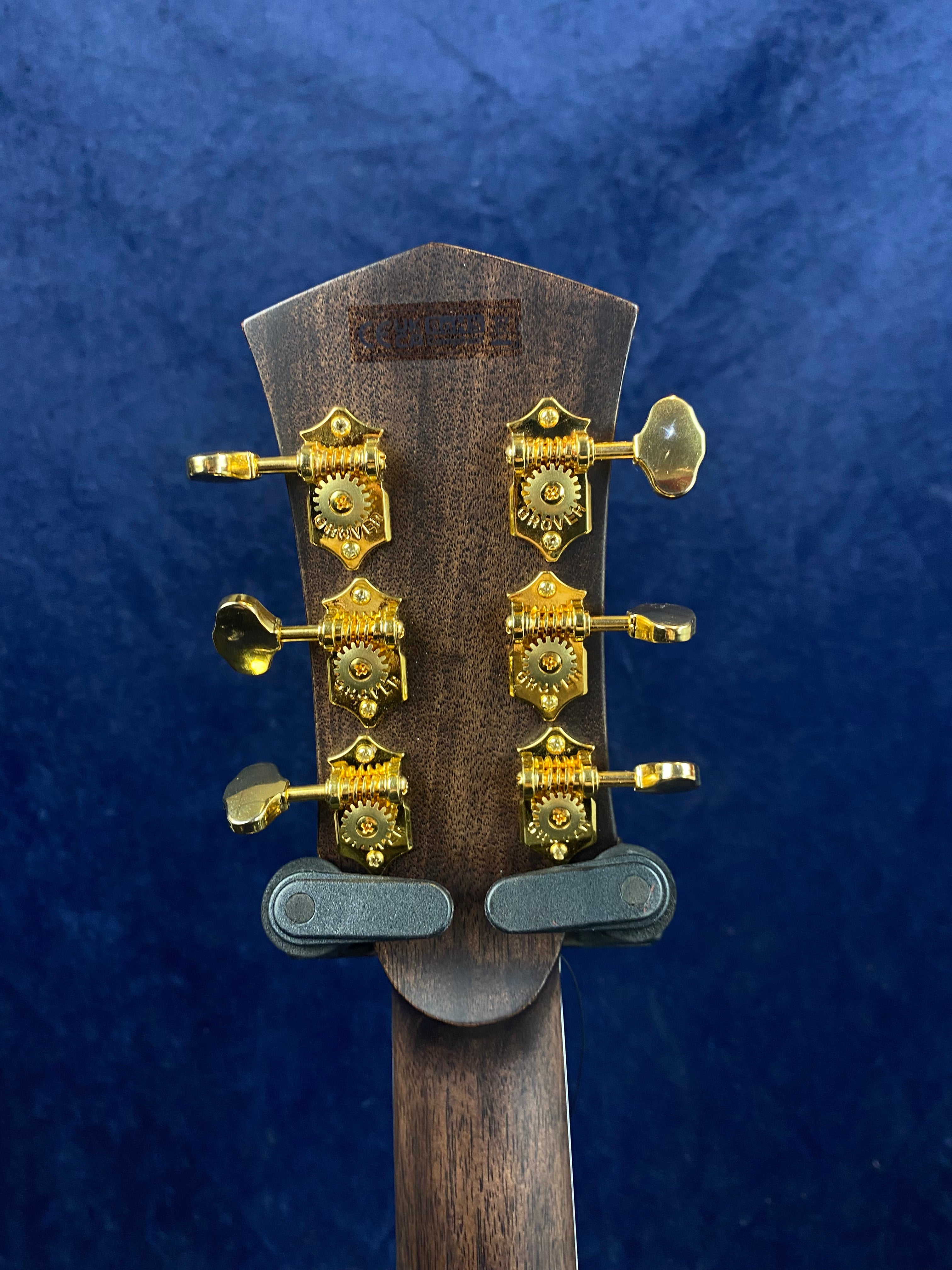 Back of an acoustic guitar headstock with six gold tuning pegs against a deep blue background.