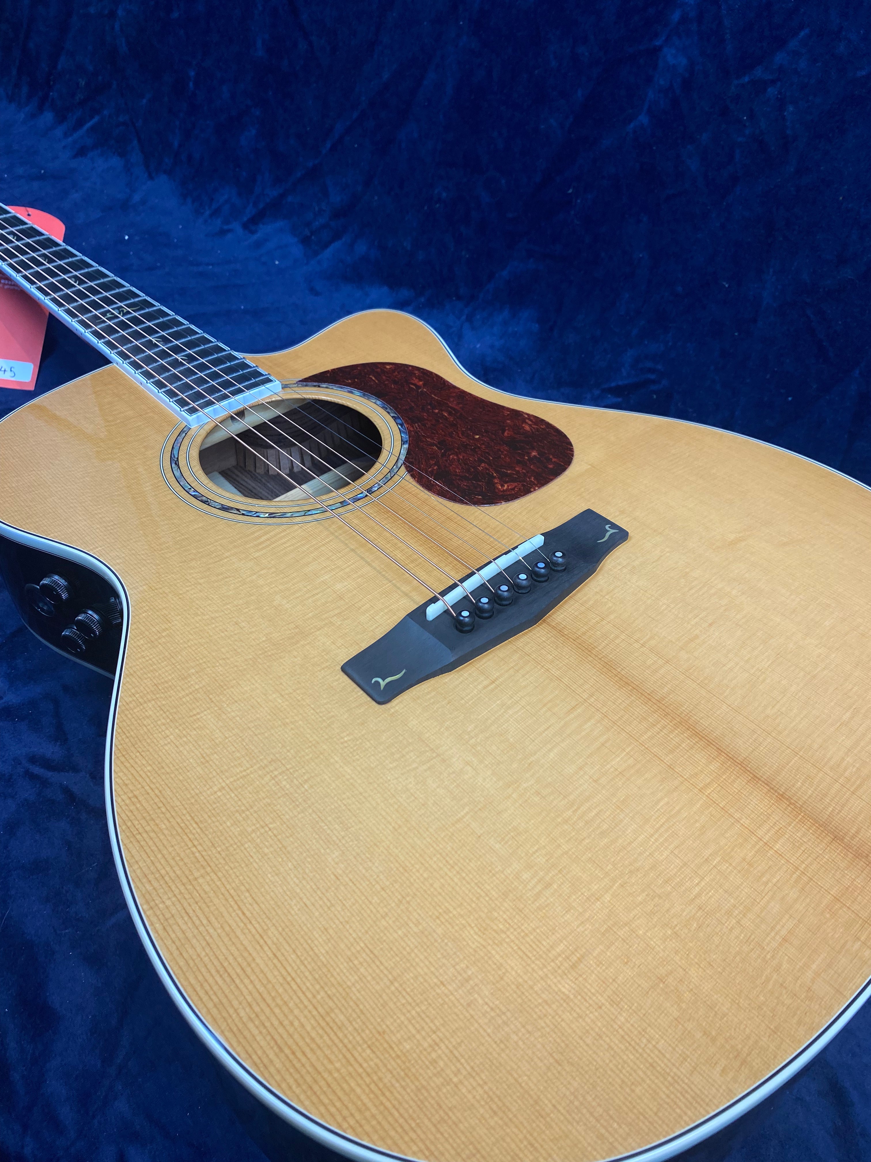 Natural wood acoustic guitar with a dark tortoiseshell pickguard, six strings, and black bridge set against a dark blue background.