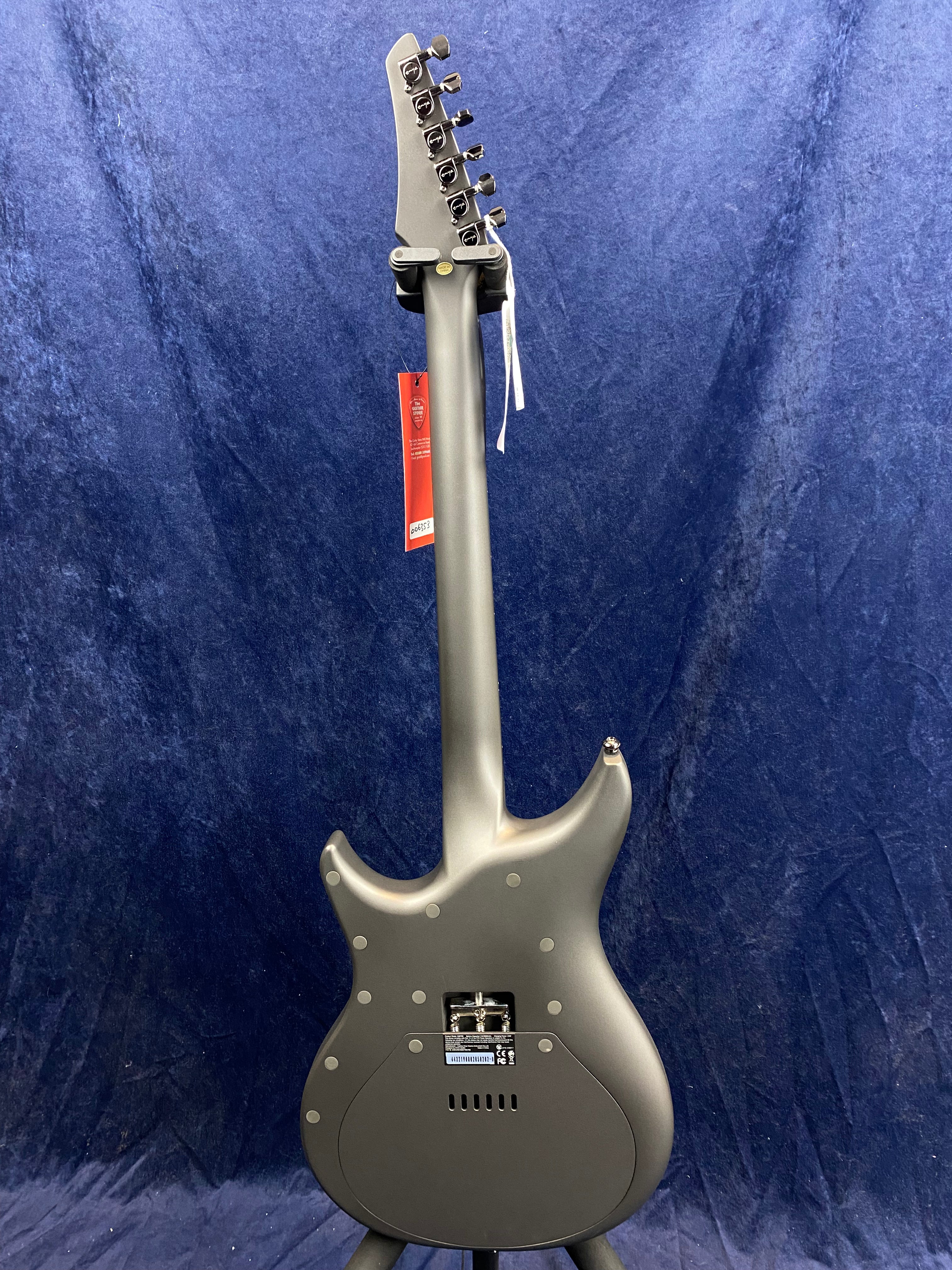 Matte gray electric guitar shown from the back, revealing its smooth contoured body, rear control cavity, and black tuning pegs against a dark blue background.