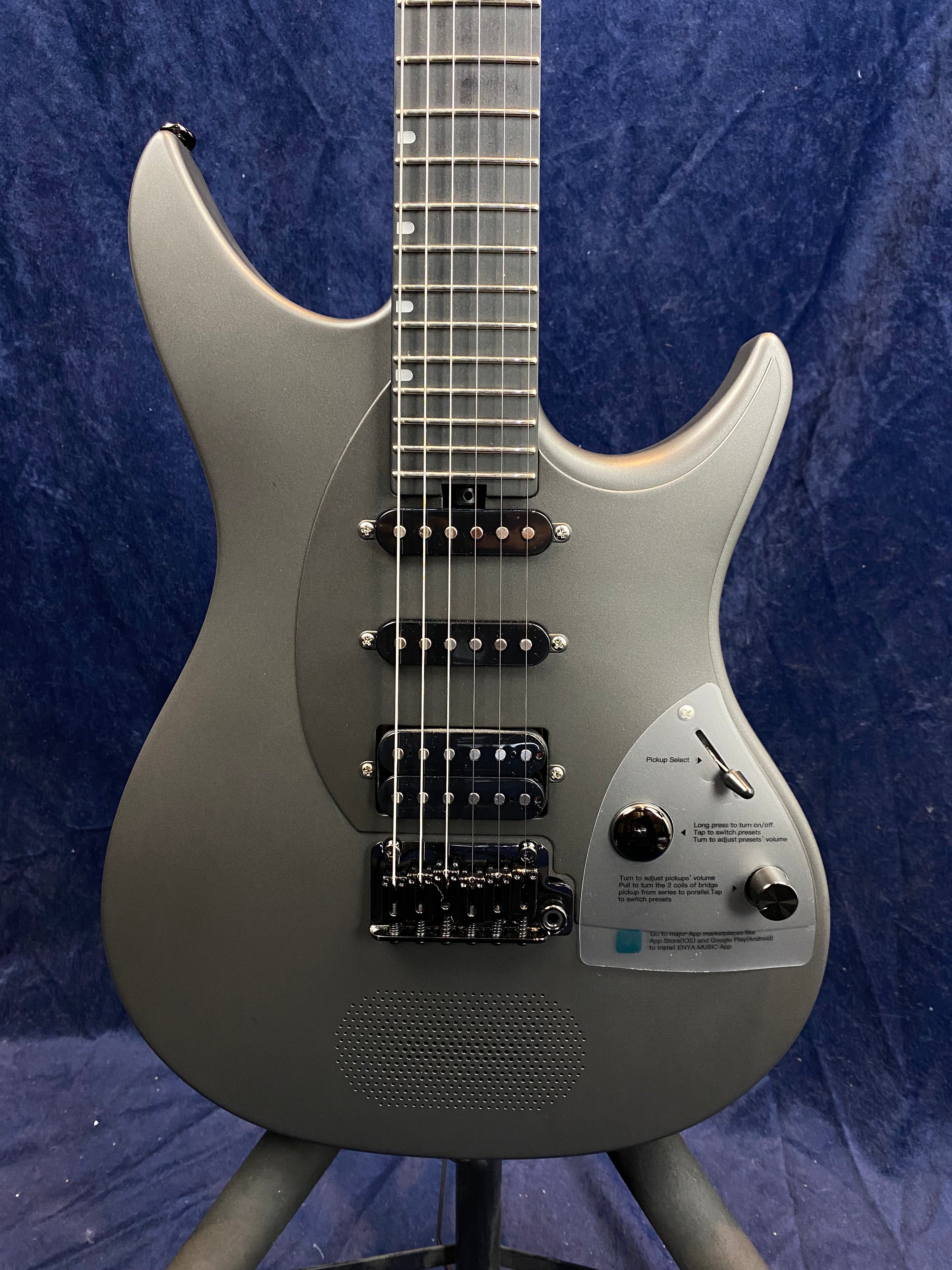 Metallic gray electric guitar with three pickups, black bridge, and knob controls on a panel with printed instructions, set against a dark blue background.