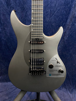 Metallic gray electric guitar with three pickups, black bridge, and knob controls on a panel with printed instructions, set against a dark blue background.