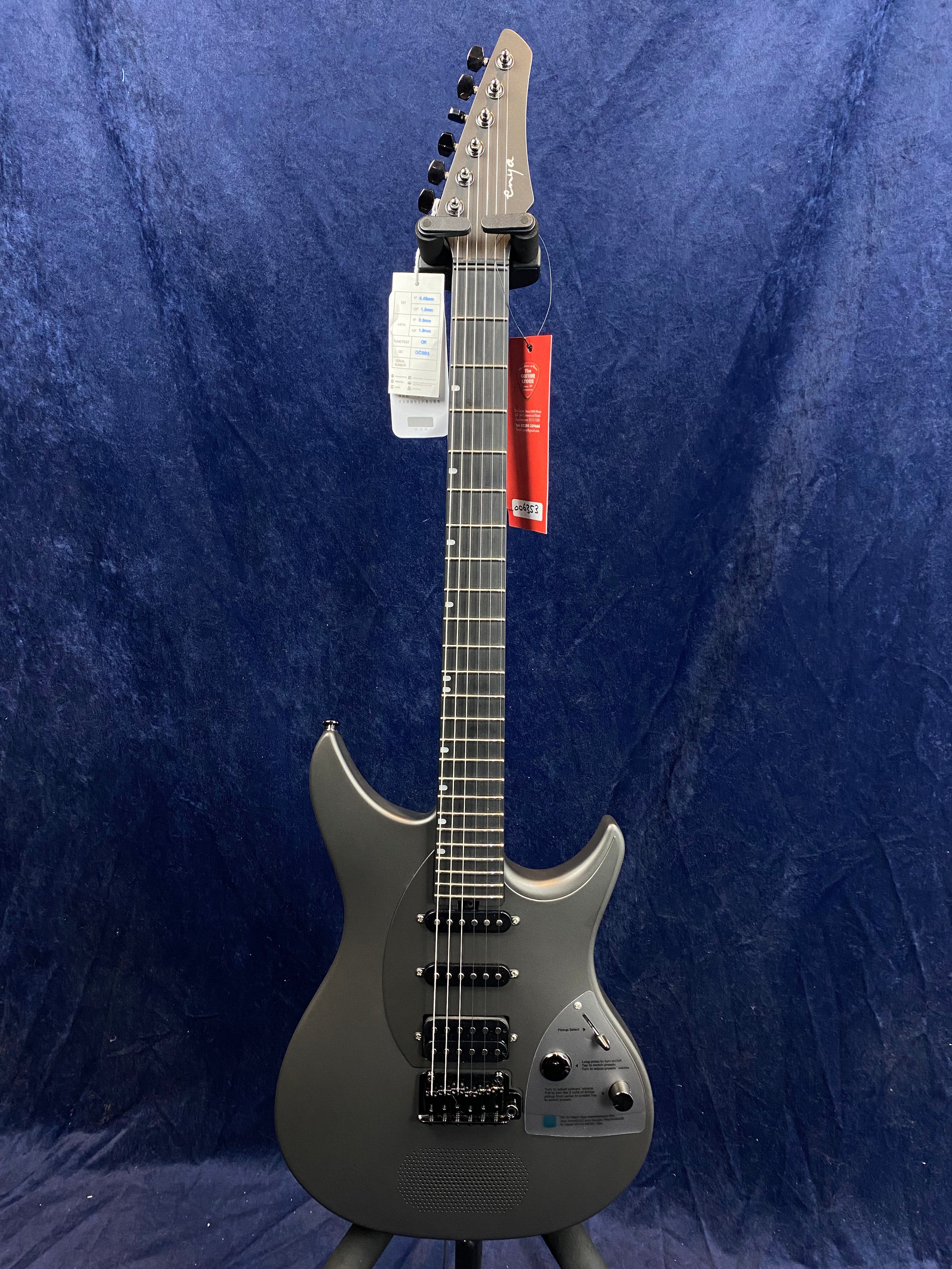 Matte gray electric guitar with a modern, contoured body, black hardware, three pickups, two control knobs, and a speaker grille near the bridge.