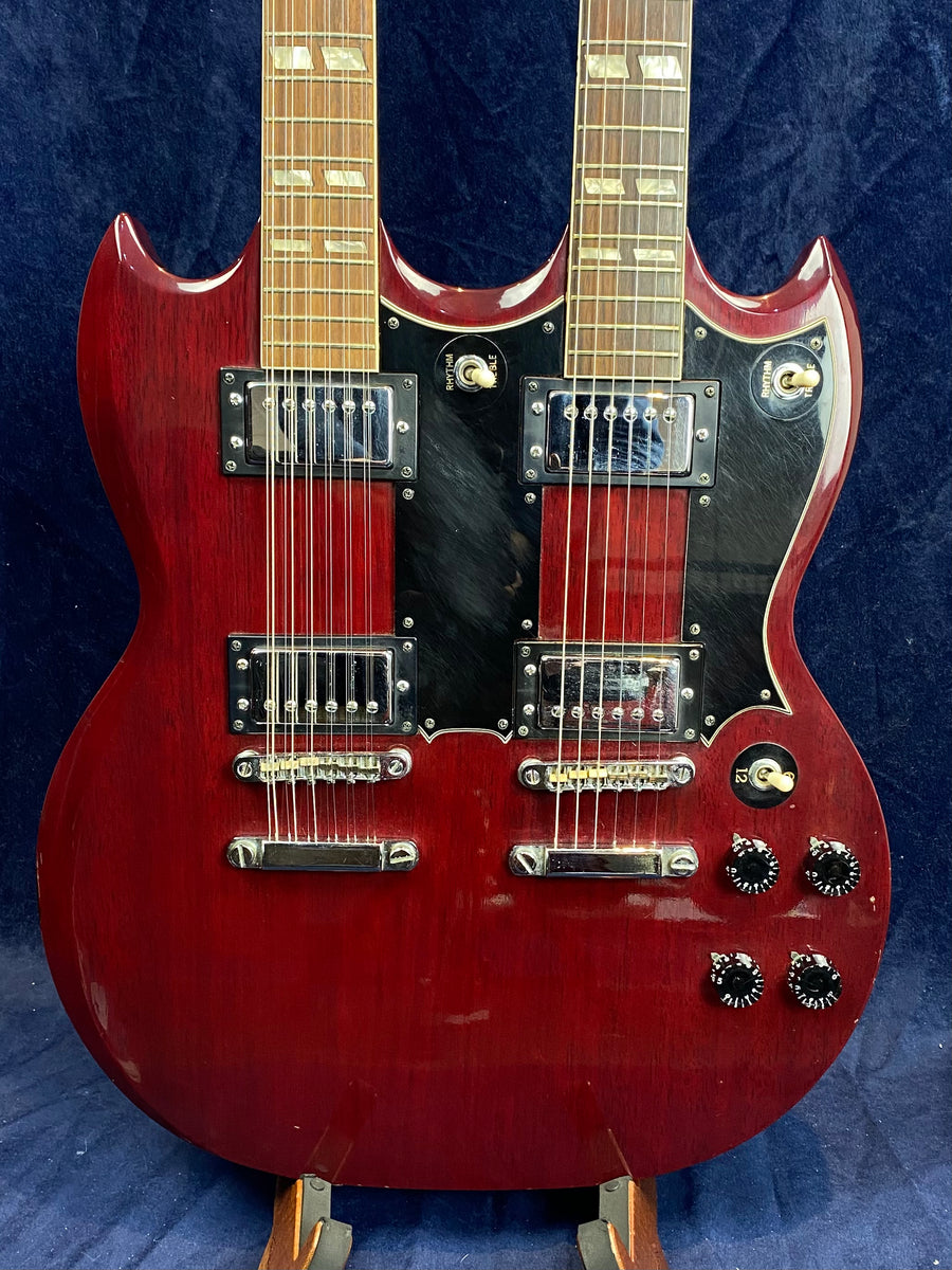 Cherry red double-neck electric guitar with two sets of pickups, knobs, and switches, mounted on a stand against a dark background.