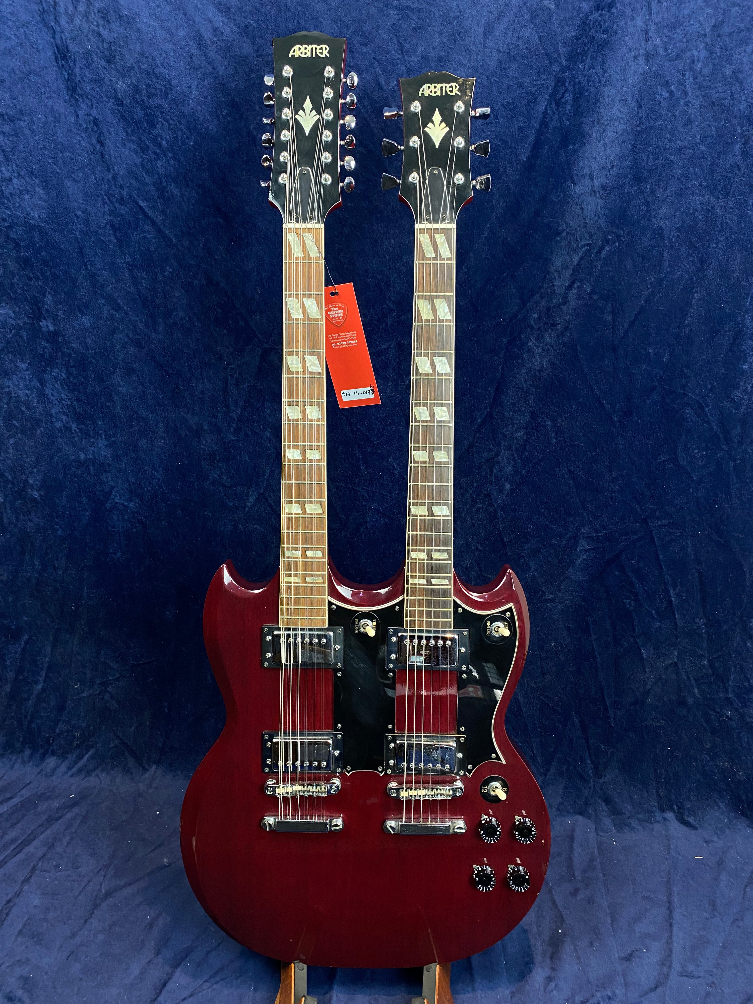 Arbiter double-neck electric guitar with a cherry red finish, two sets of pickups, and black pickguards against a dark blue background.
