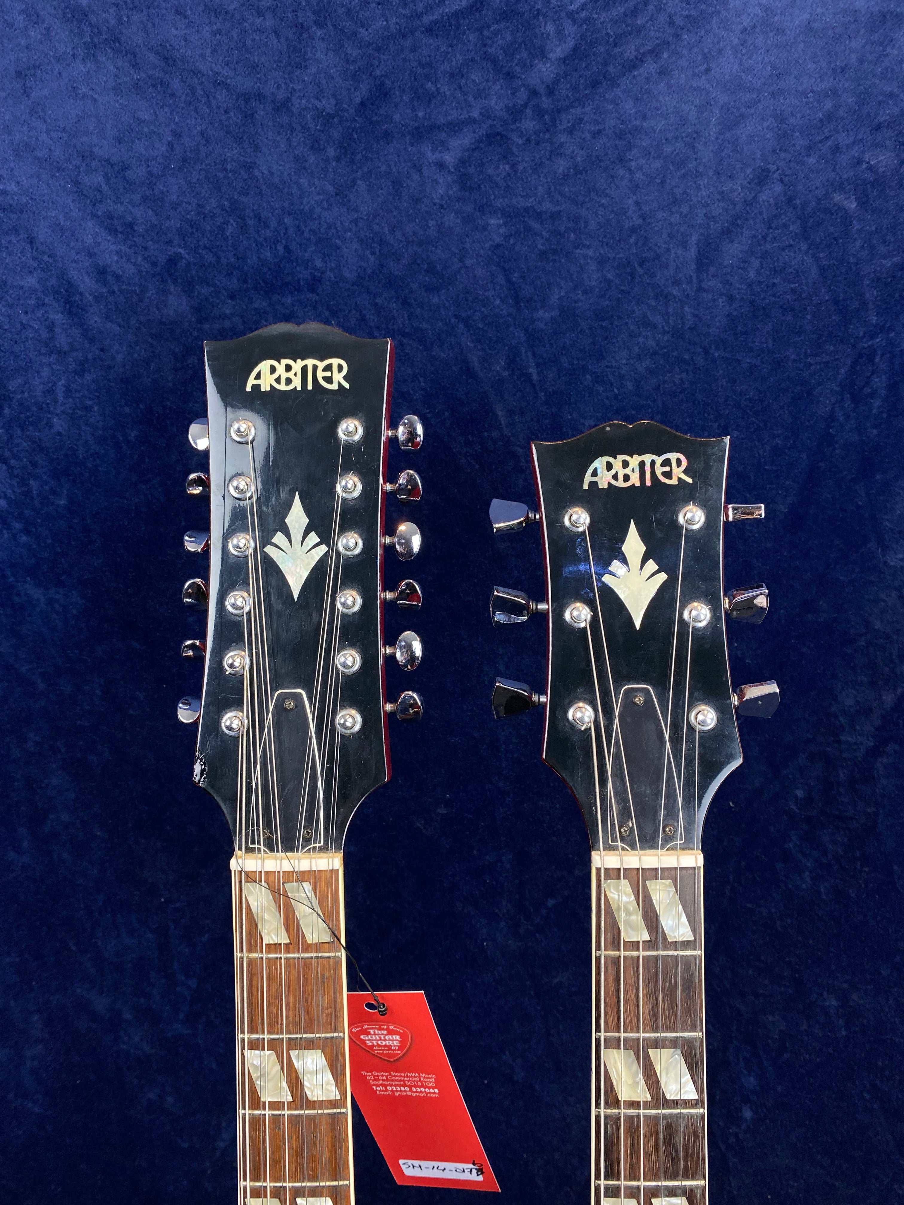 Two Arbiter electric guitar headstocks side by side, both with inlaid designs and tuning pegs, against a dark blue background.