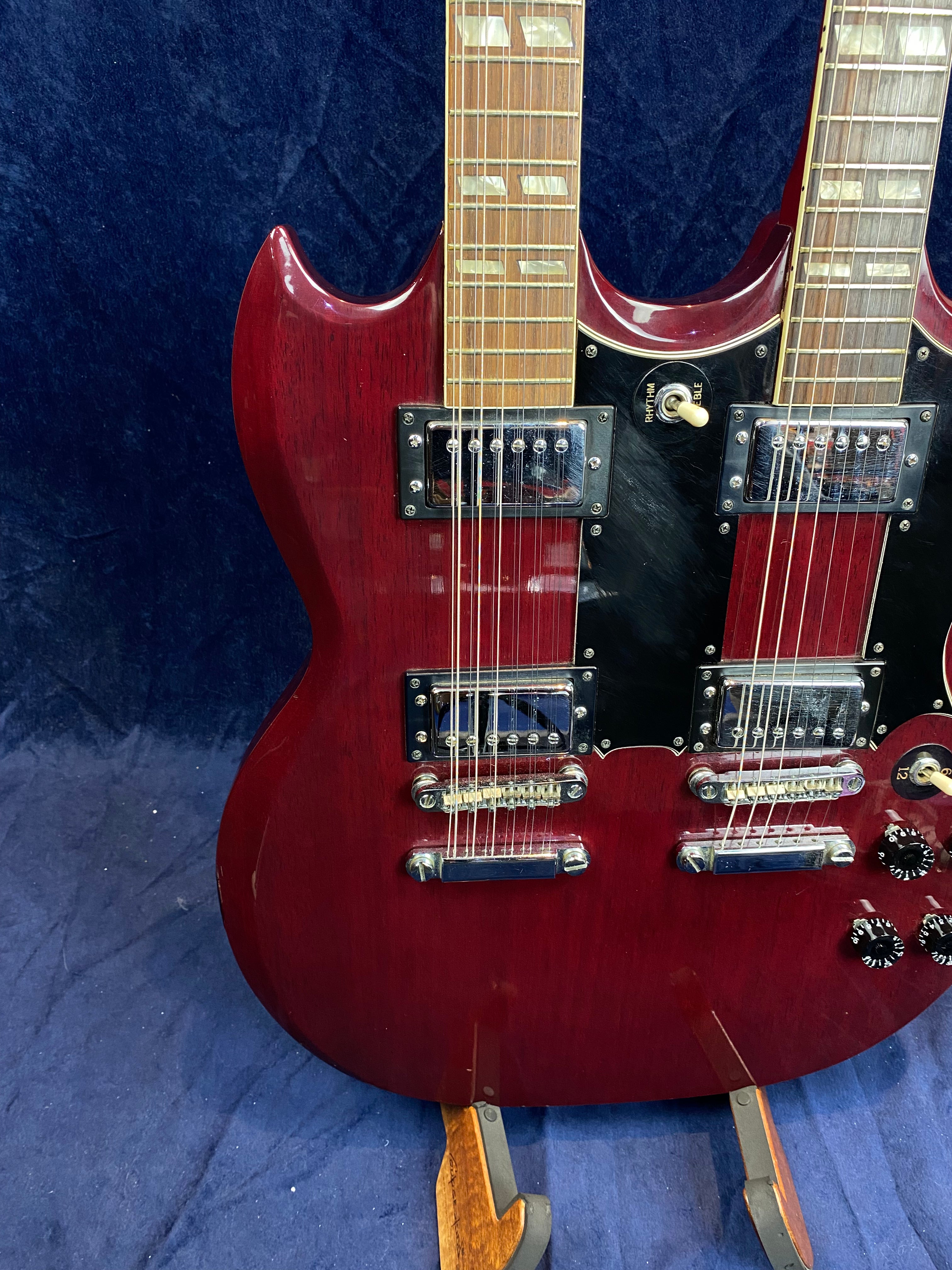 Cherry red double-neck electric guitar with two sets of pickups, switches, and knobs, displayed upright against a dark blue background.