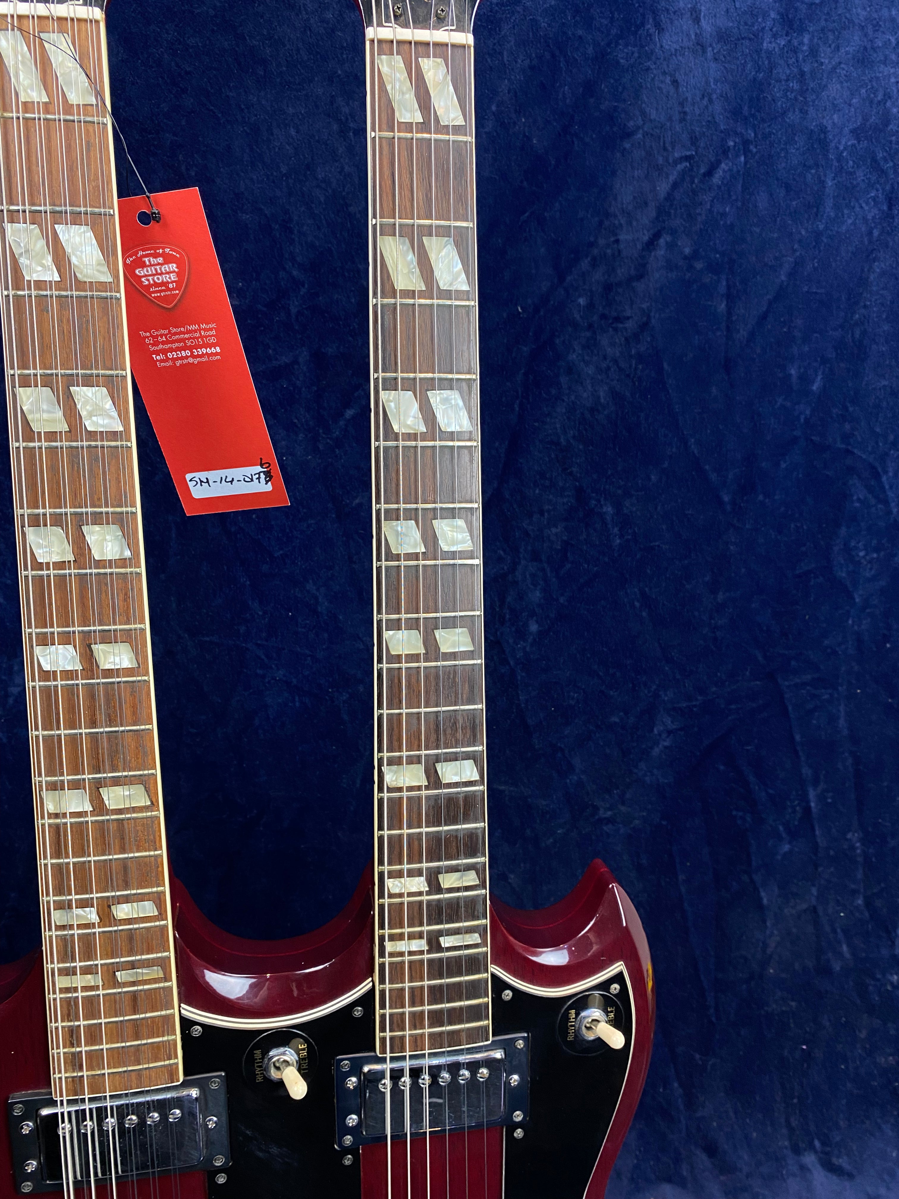 Two cherry red double-neck electric guitars side by side, each with rectangular inlays and separate pickups, against a dark blue background.