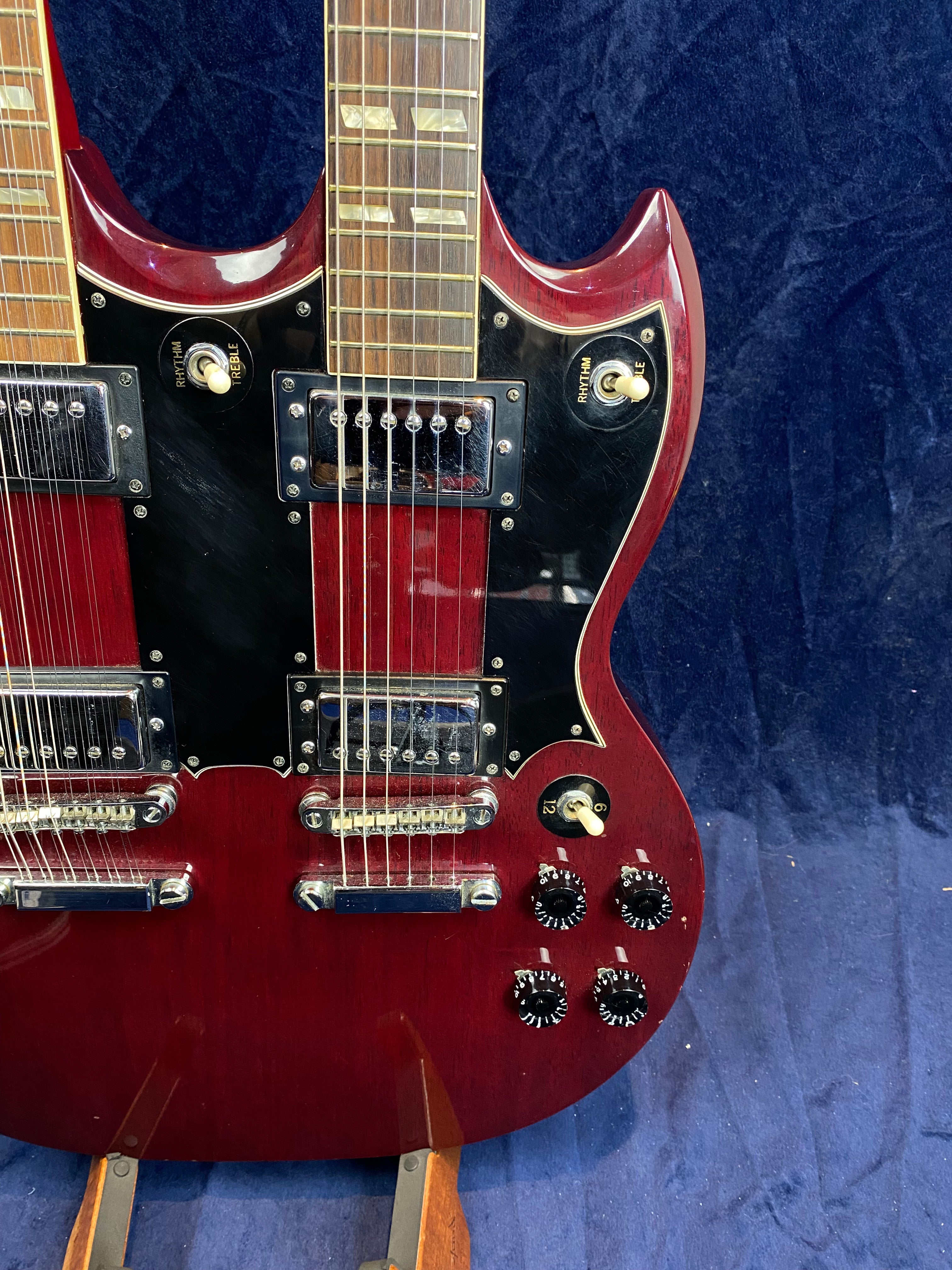 Double-neck electric guitar in deep red finish with two sets of pickups, switches, and black control knobs against a dark blue background.