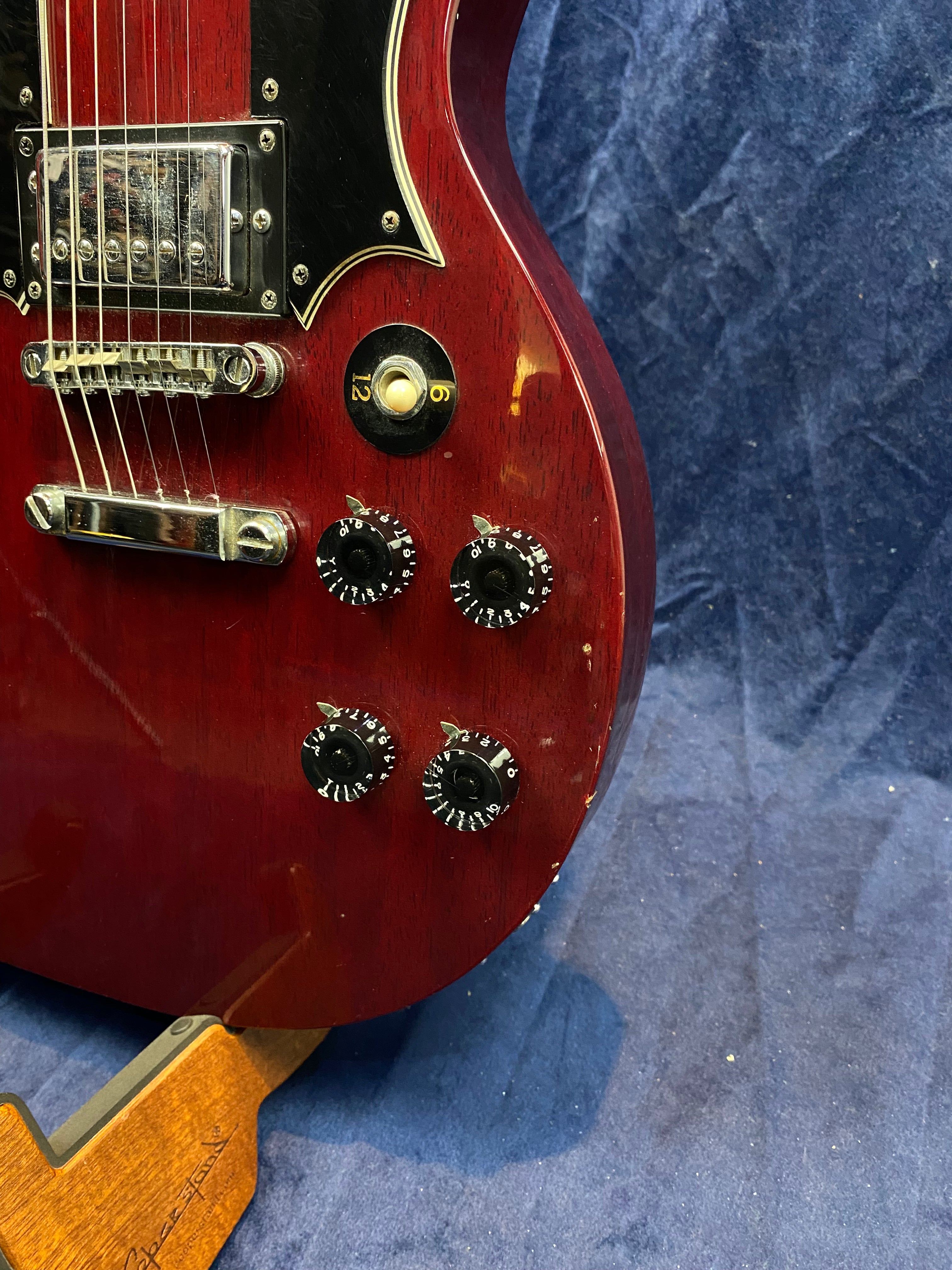 Cherry red electric guitar body with black pickguard, four black control knobs, a switch, chrome bridge, and some visible scratches and wear.