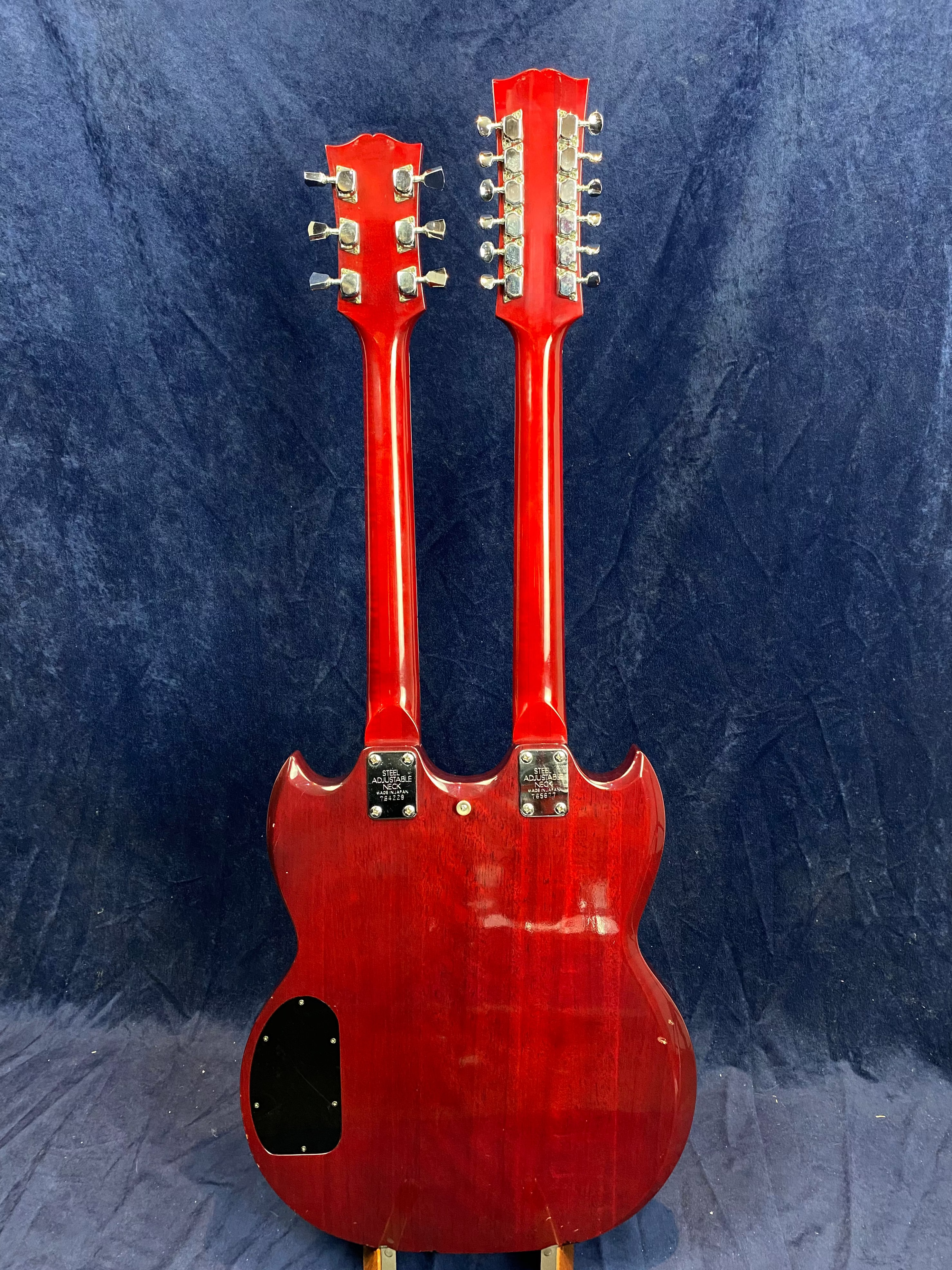 Red double-neck electric guitar shown from the back, with one neck for six strings and the other for twelve, set against a dark blue background.