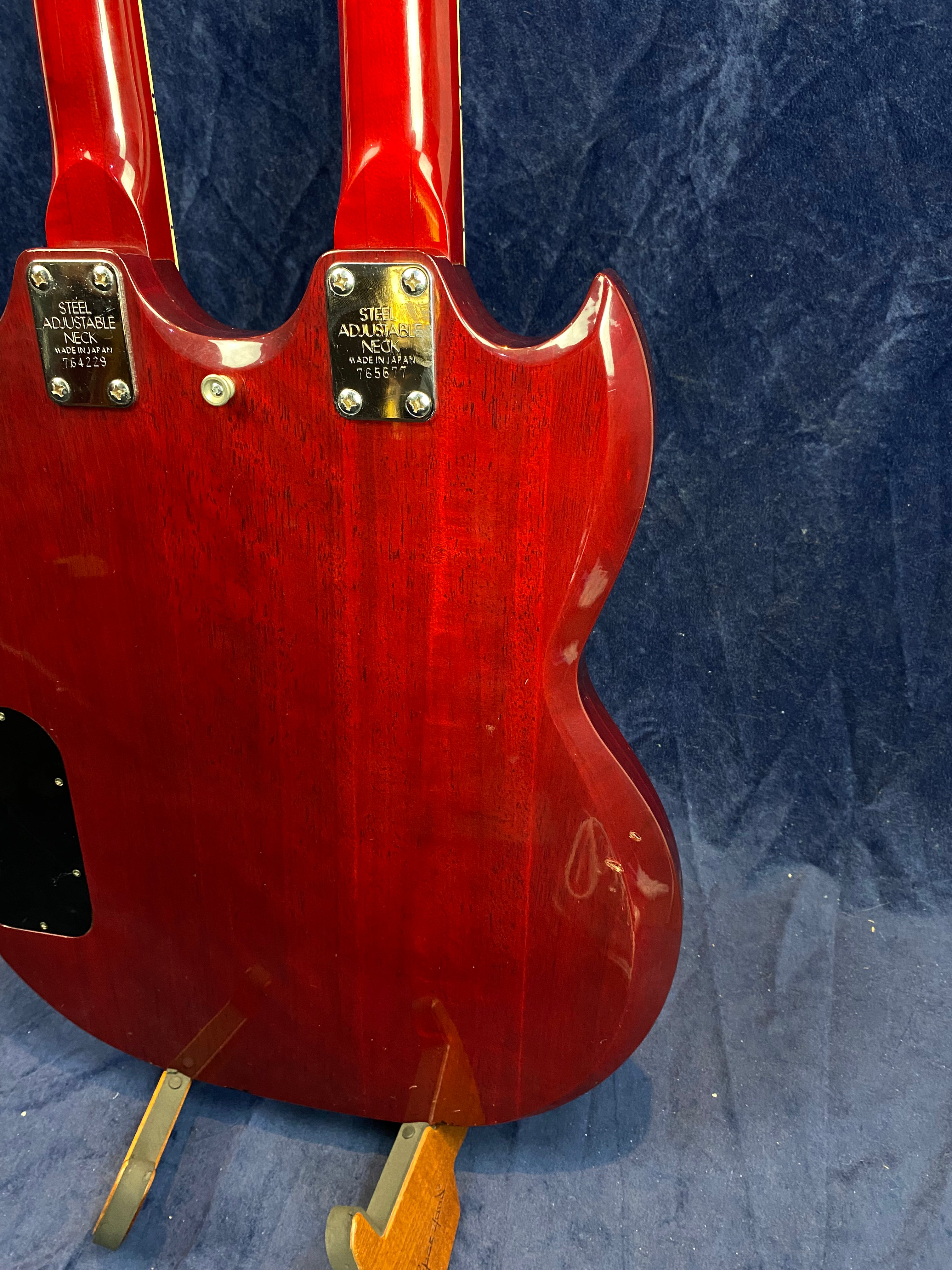 Cherry red double-neck electric guitar with steel adjustable neck plates and serial numbers, shown from the back against a dark blue background.