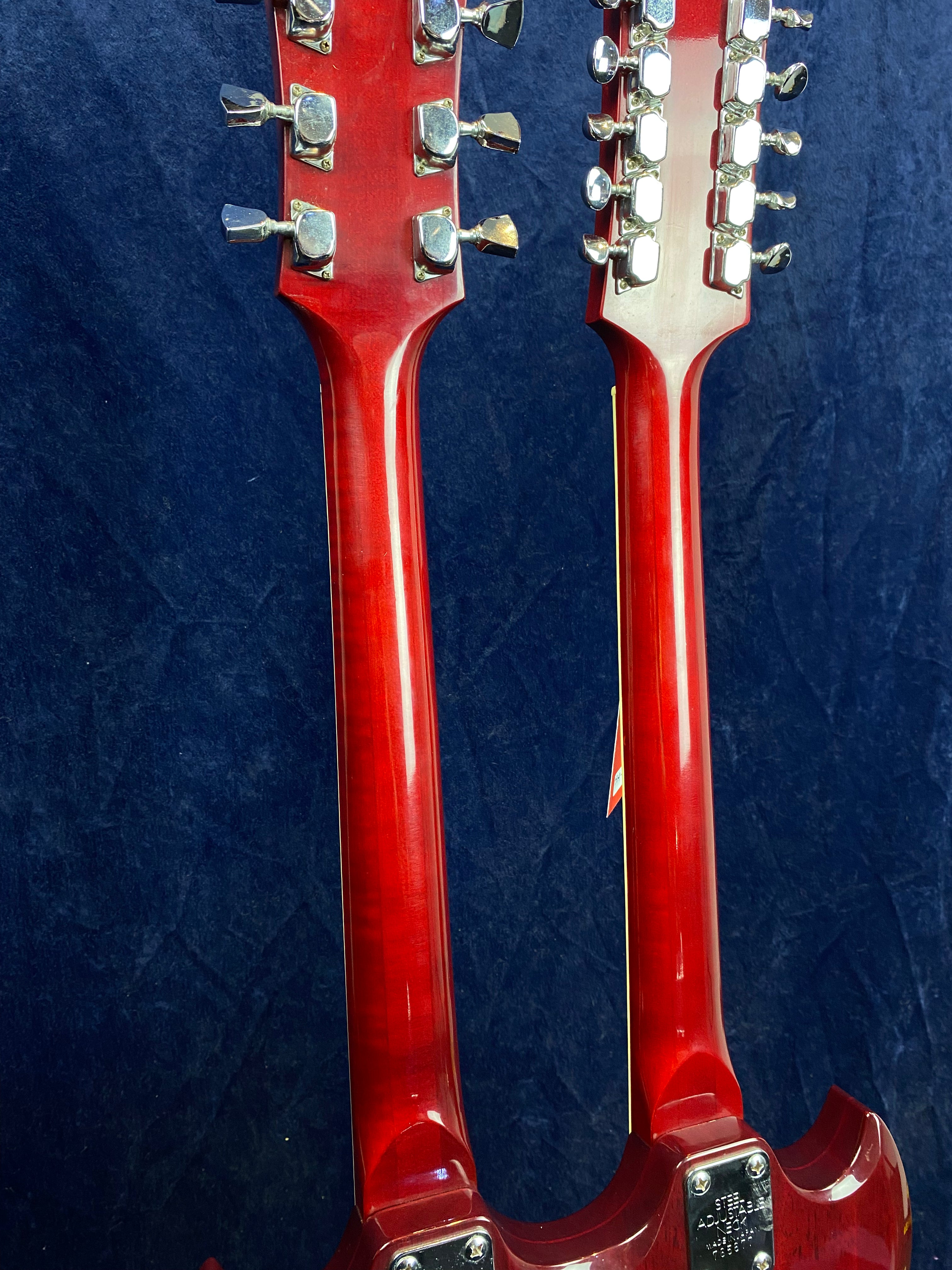 Two red electric guitars joined at the body, each with chrome tuning pegs and separate necks, shown from the back against a dark background.