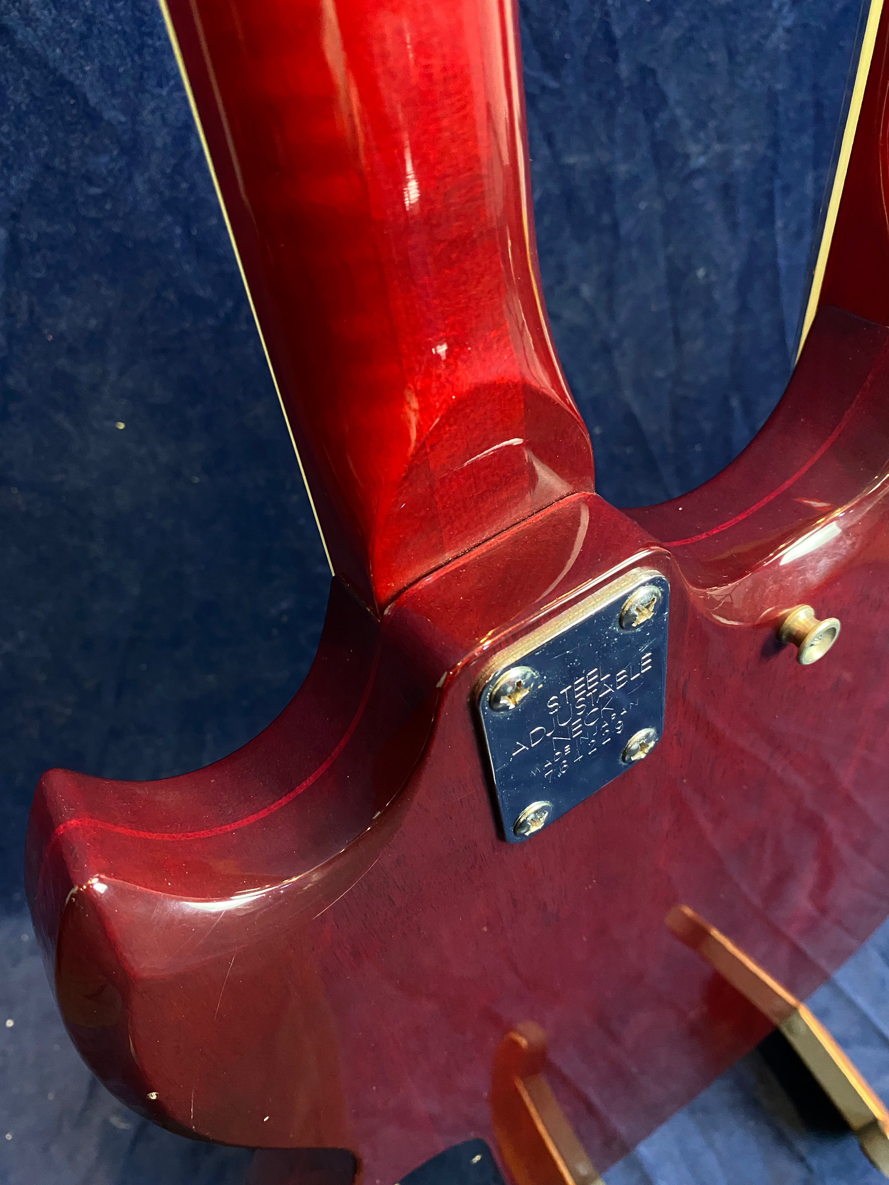 Glossy red electric guitar body and neck joint, with a metal plate labeled "Steel Adjustable Neck" fastened by four screws.