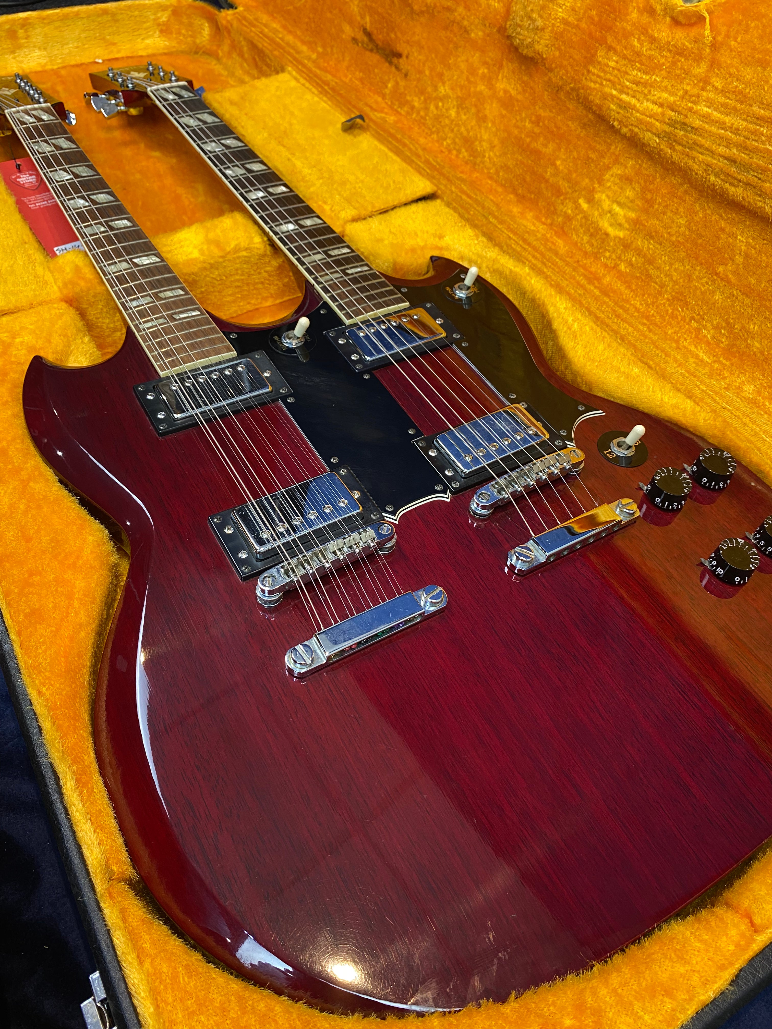 Red double-neck electric guitar with chrome hardware and black pickguards, resting inside a yellow velvet-lined case.