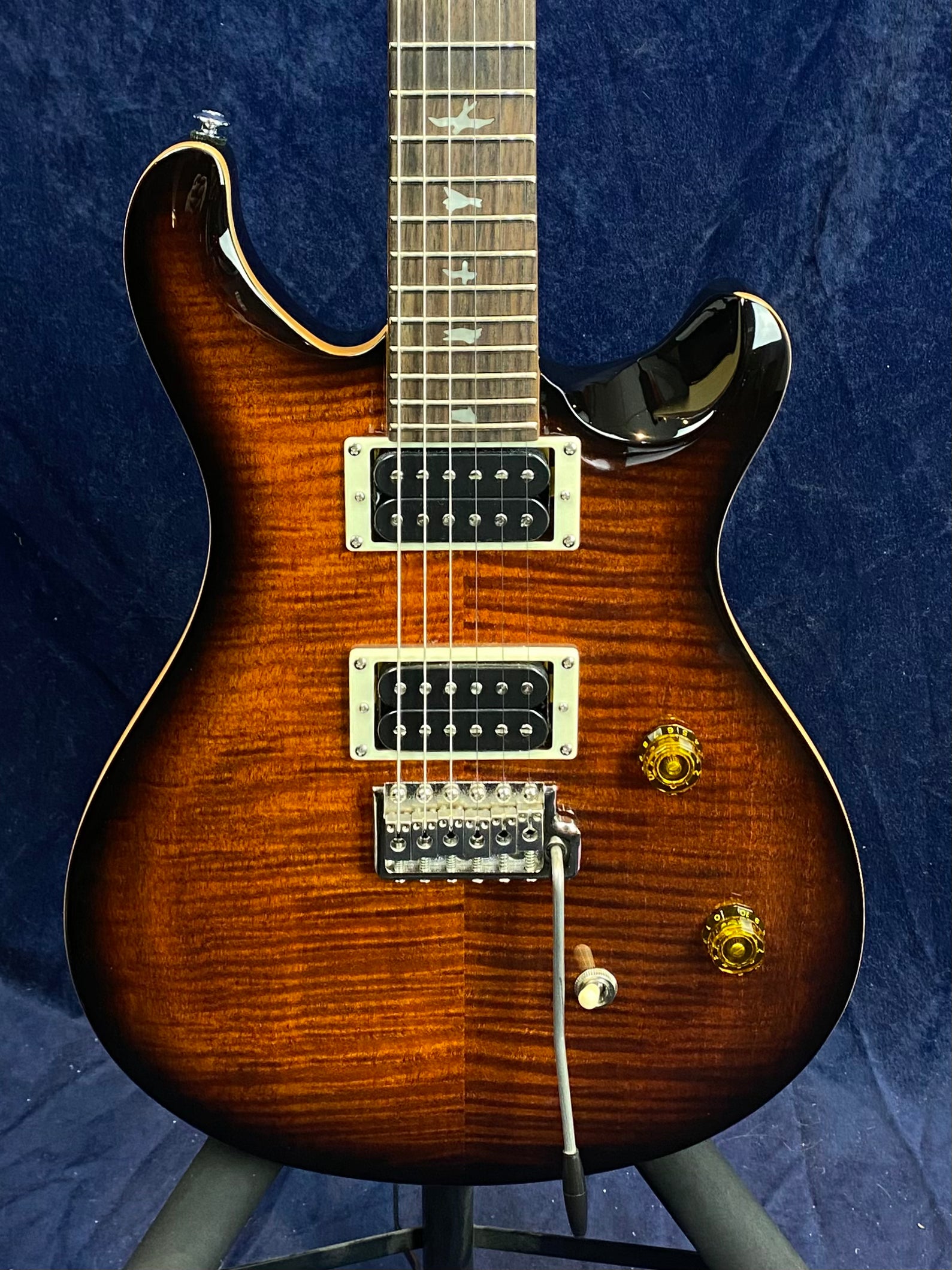 Electric guitar with a brown sunburst finish, two humbucker pickups, tremolo bridge, two amber knobs, and bird inlays on the fretboard.