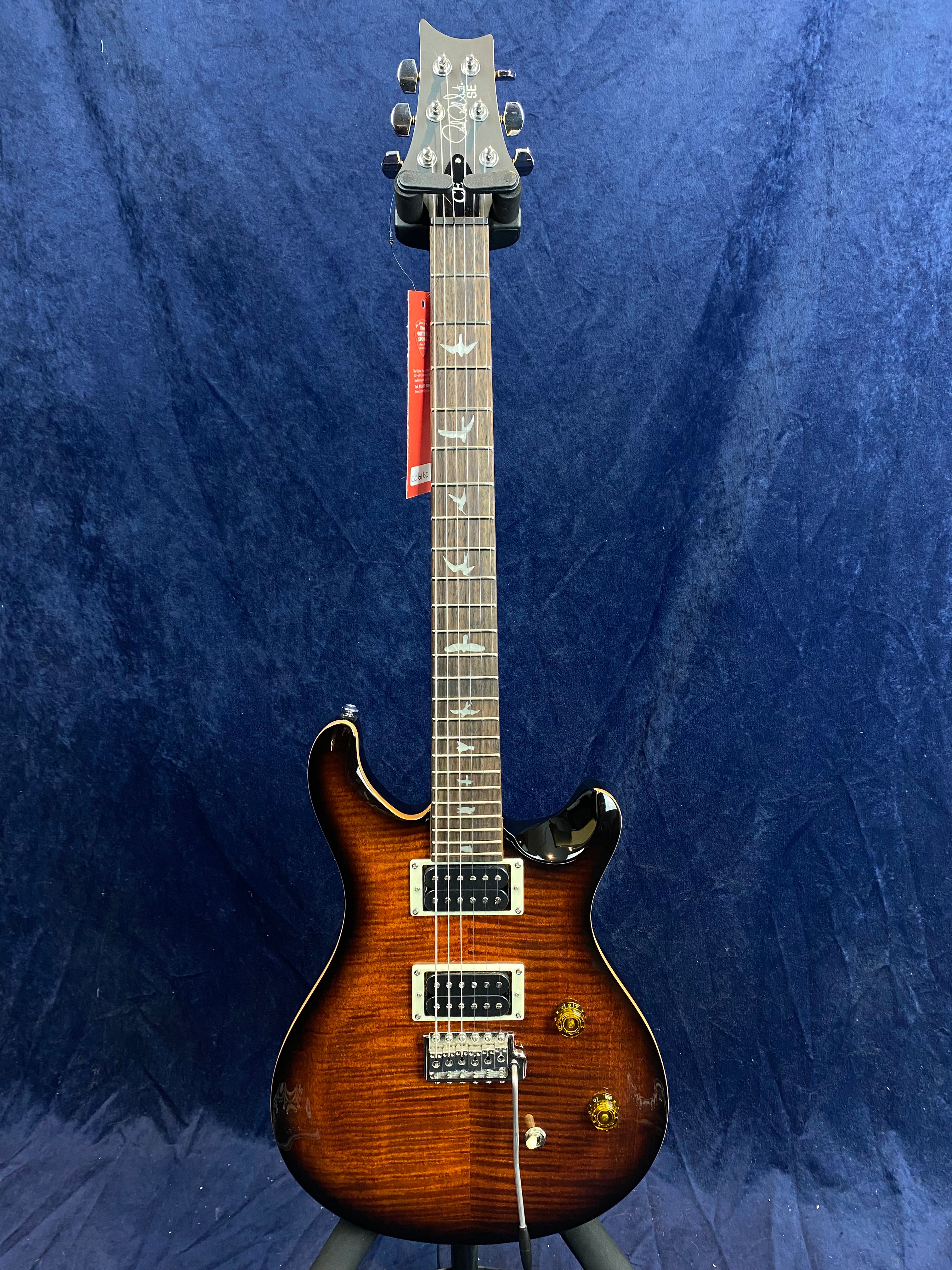 Sunburst finish electric guitar with dual humbucker pickups, three control knobs, and bird inlays on the fretboard, shown on a stand against a blue background.