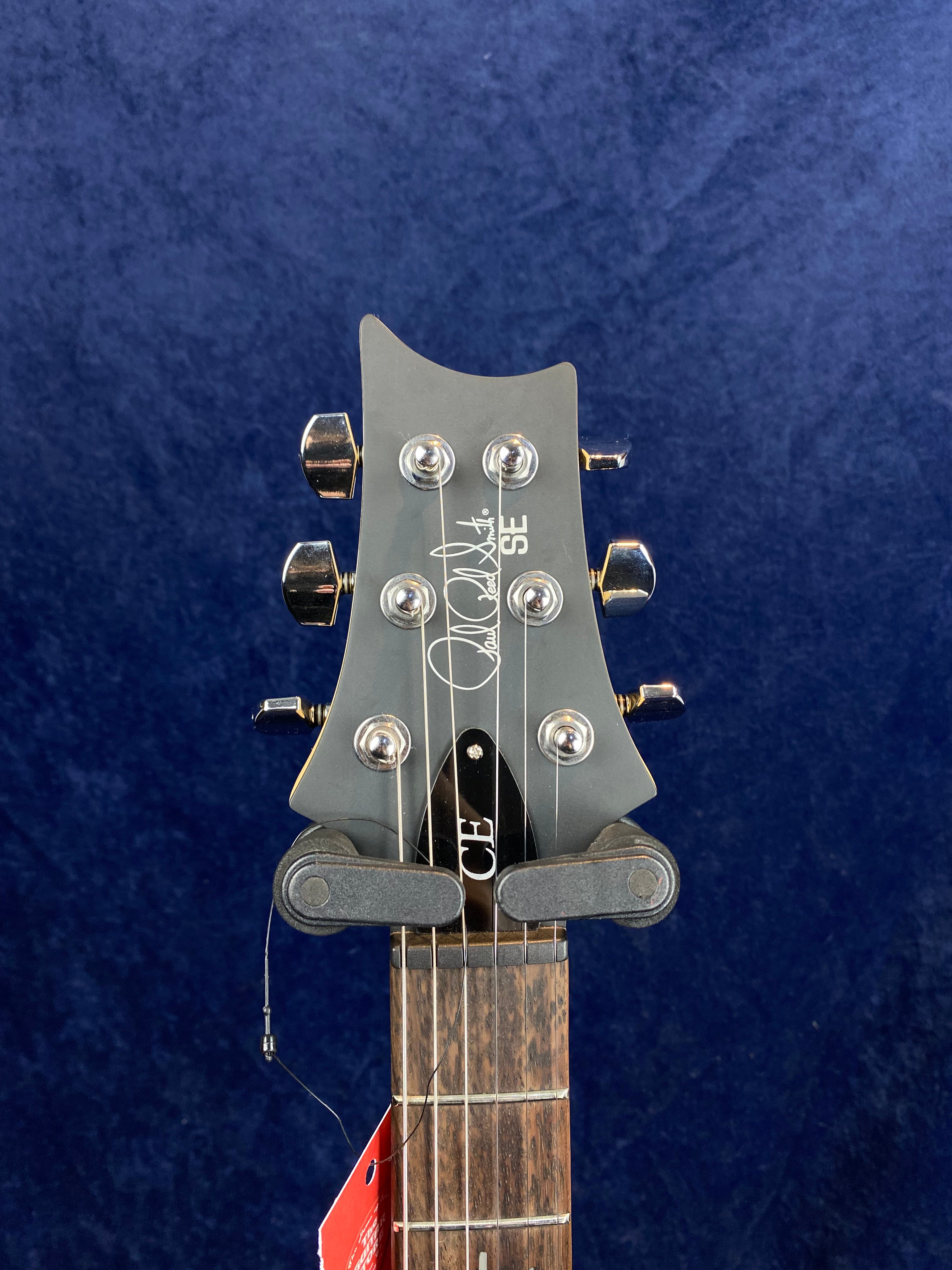 Headstock of a PRS SE electric guitar with six chrome tuning pegs, visible signature logo, and part of a dark wood fretboard.