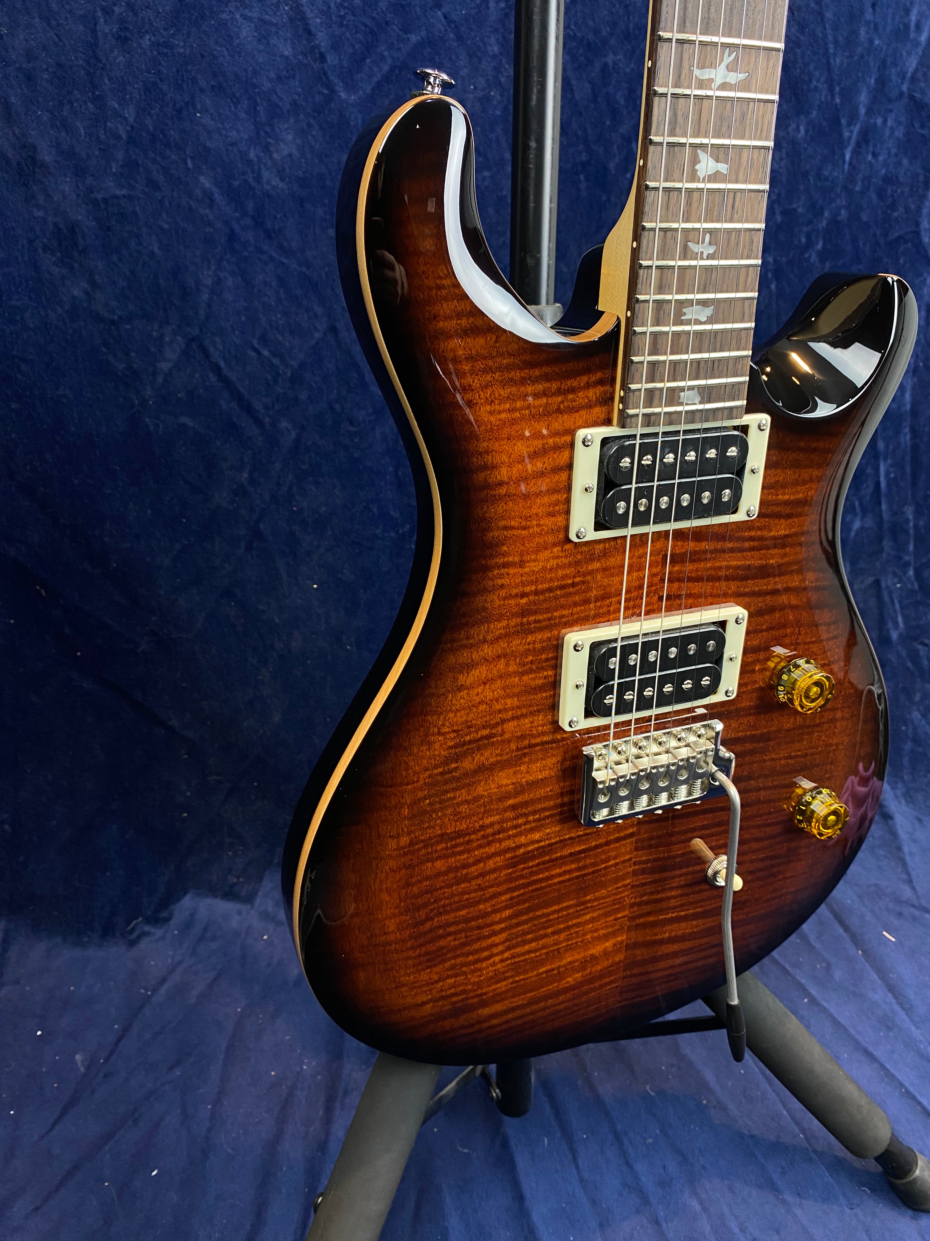 Sunburst electric guitar with dual humbucker pickups, two amber knobs, a tremolo bridge, and bird-shaped fret inlays on a rosewood fretboard.