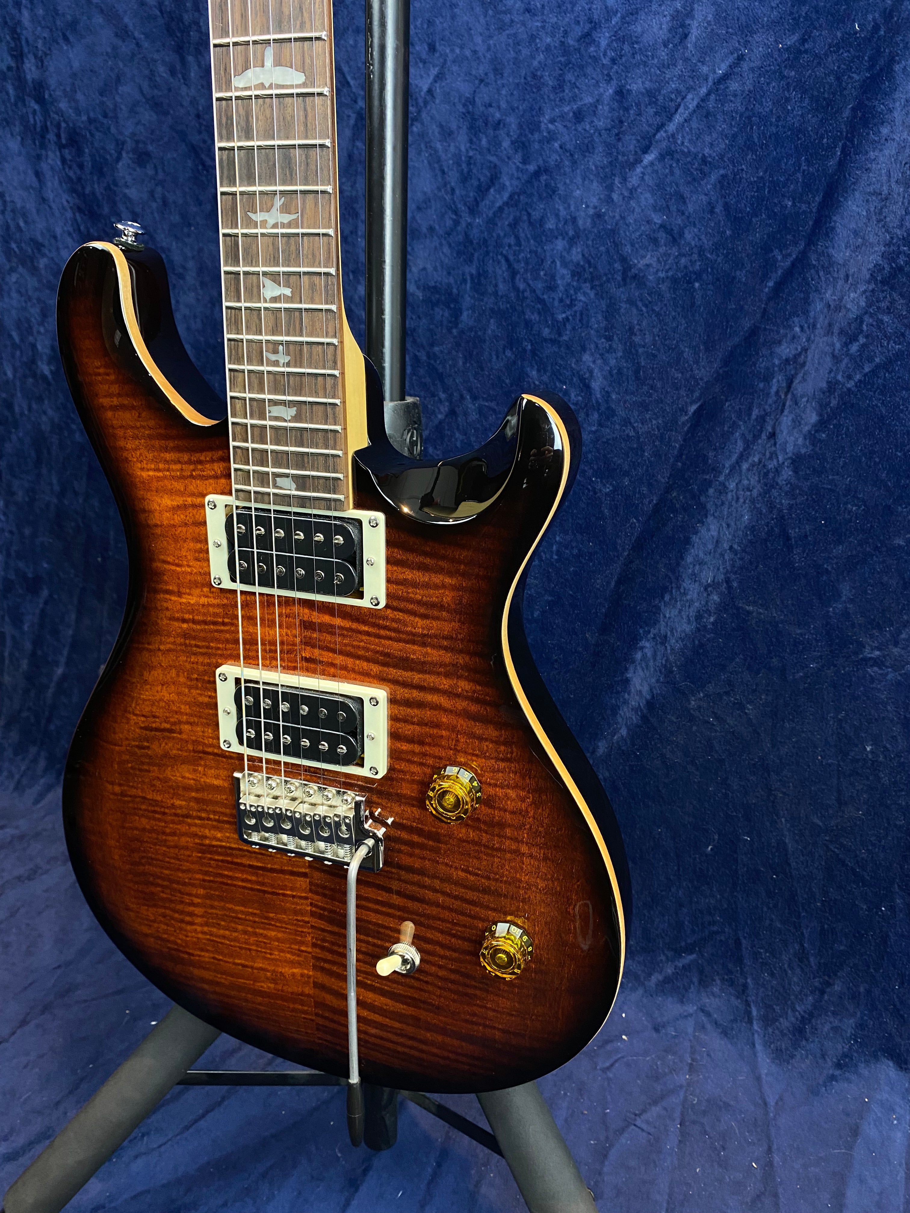 Electric guitar with a glossy brown sunburst finish, two humbucker pickups, two knobs, a switch, and a tremolo bar. Bird inlays decorate the fretboard.