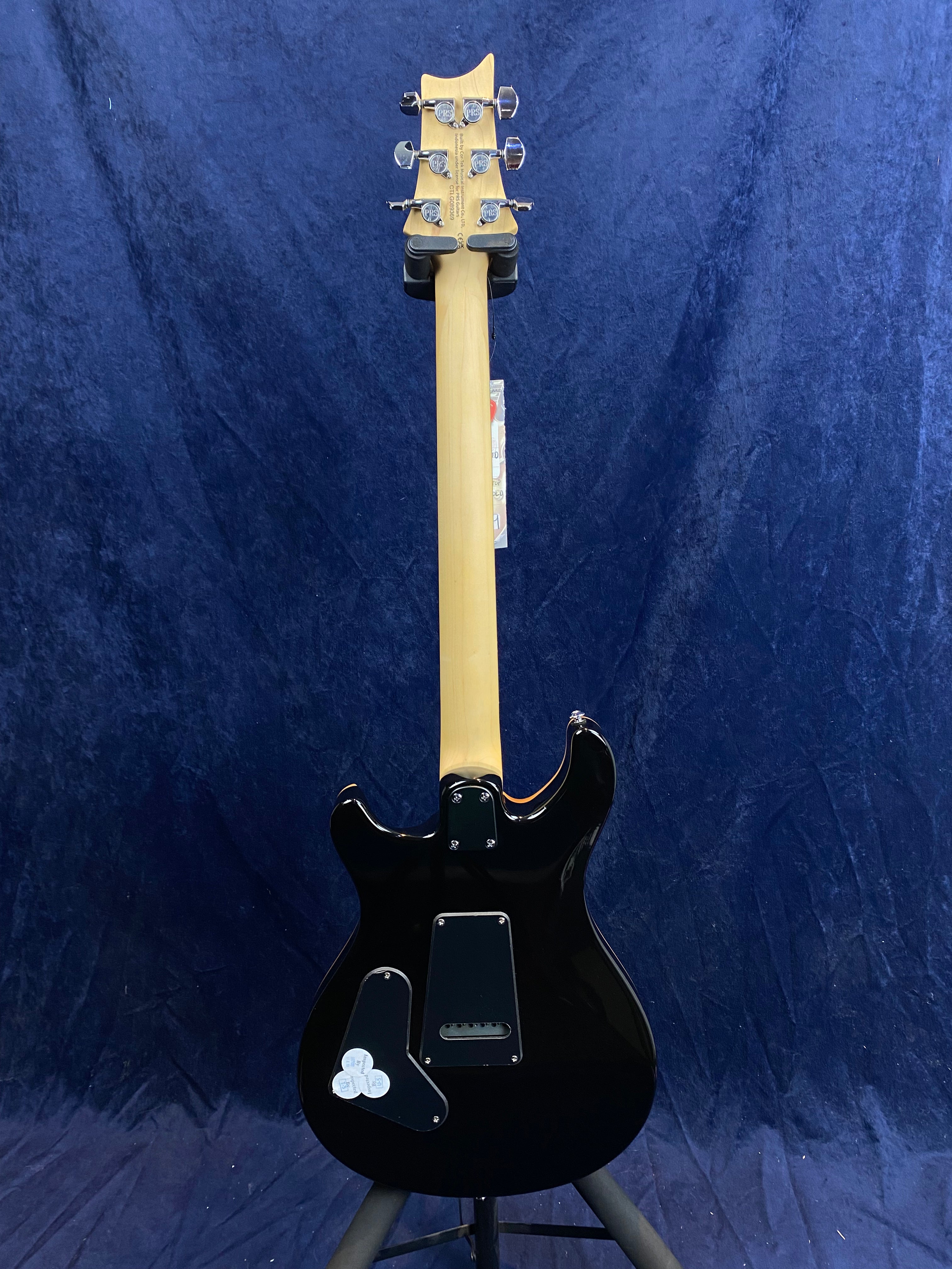 Electric guitar seen from the back, featuring a natural wood neck, black body with access panels, and three white picks attached near the bottom.
