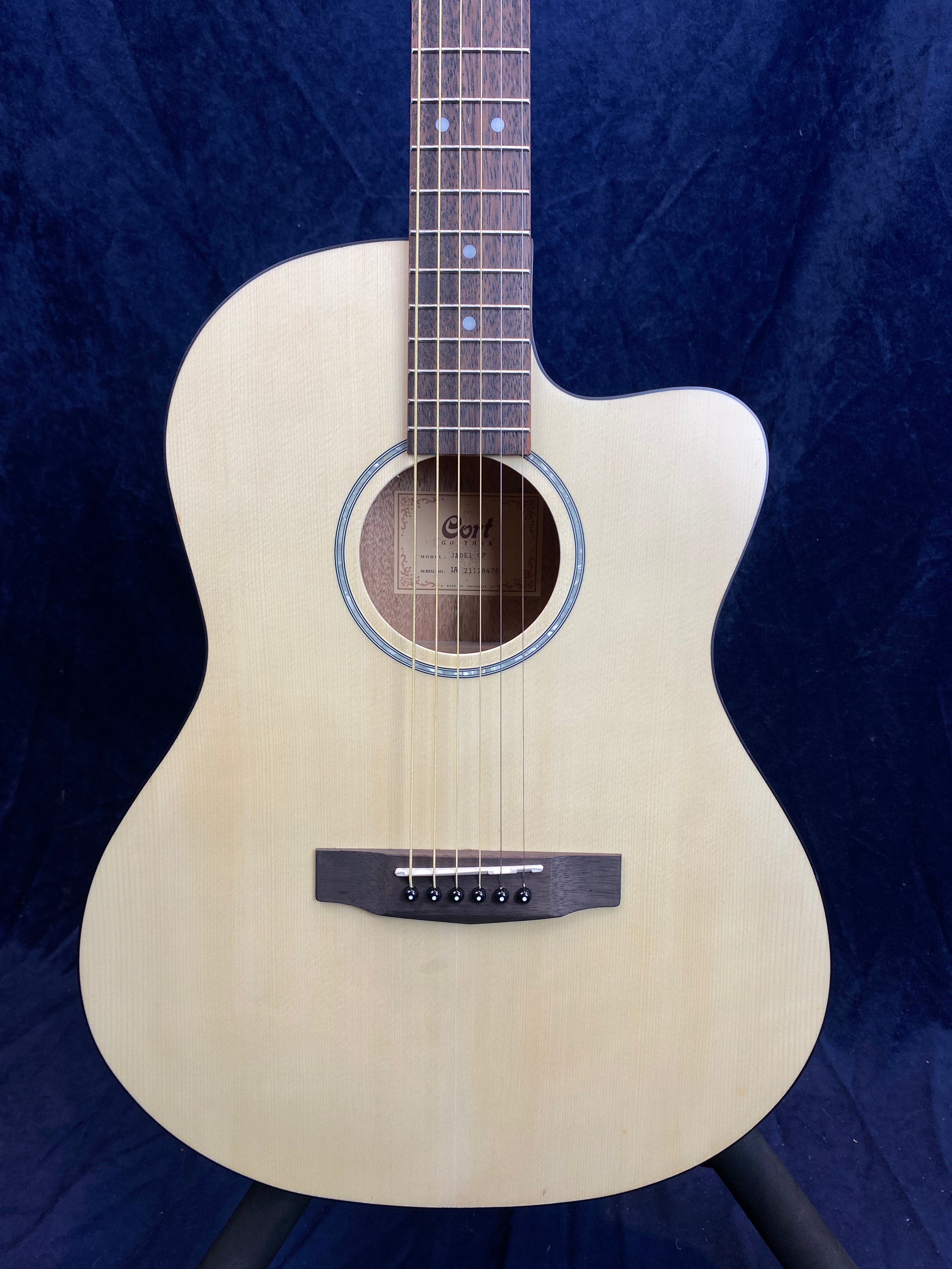 Guitare acoustique à pan coupé, table claire, rosace simple, chevalet foncé à six chevilles noires, touche marquée de repères ronds blancs.