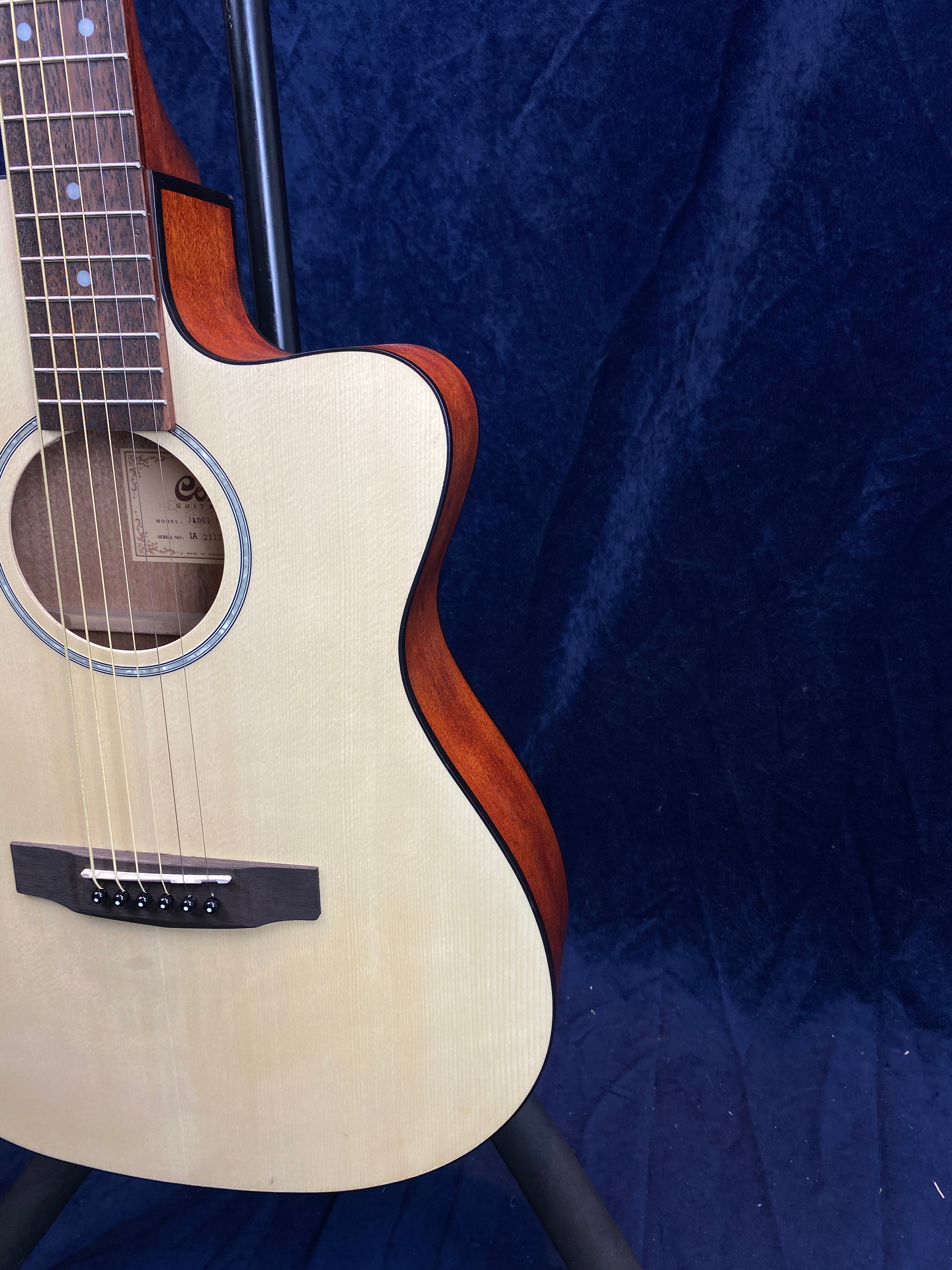 Light wood acoustic guitar with a cutaway design, dark wood sides, visible strings, and bridge, set against a dark blue textured background.
