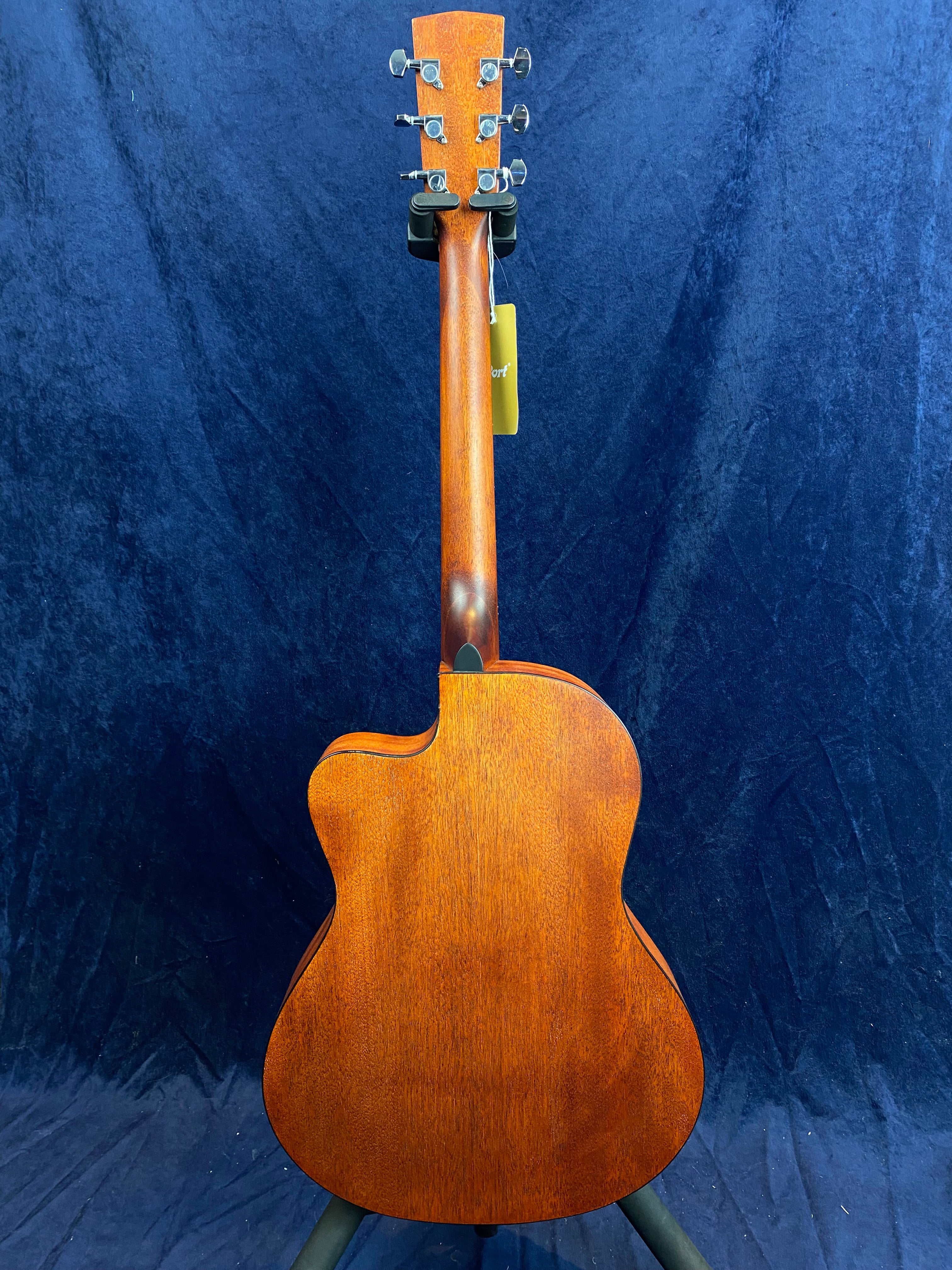 Acoustic guitar seen from the back, showing a warm brown wooden finish, six tuning pegs, and a cutaway body shape against a dark background.