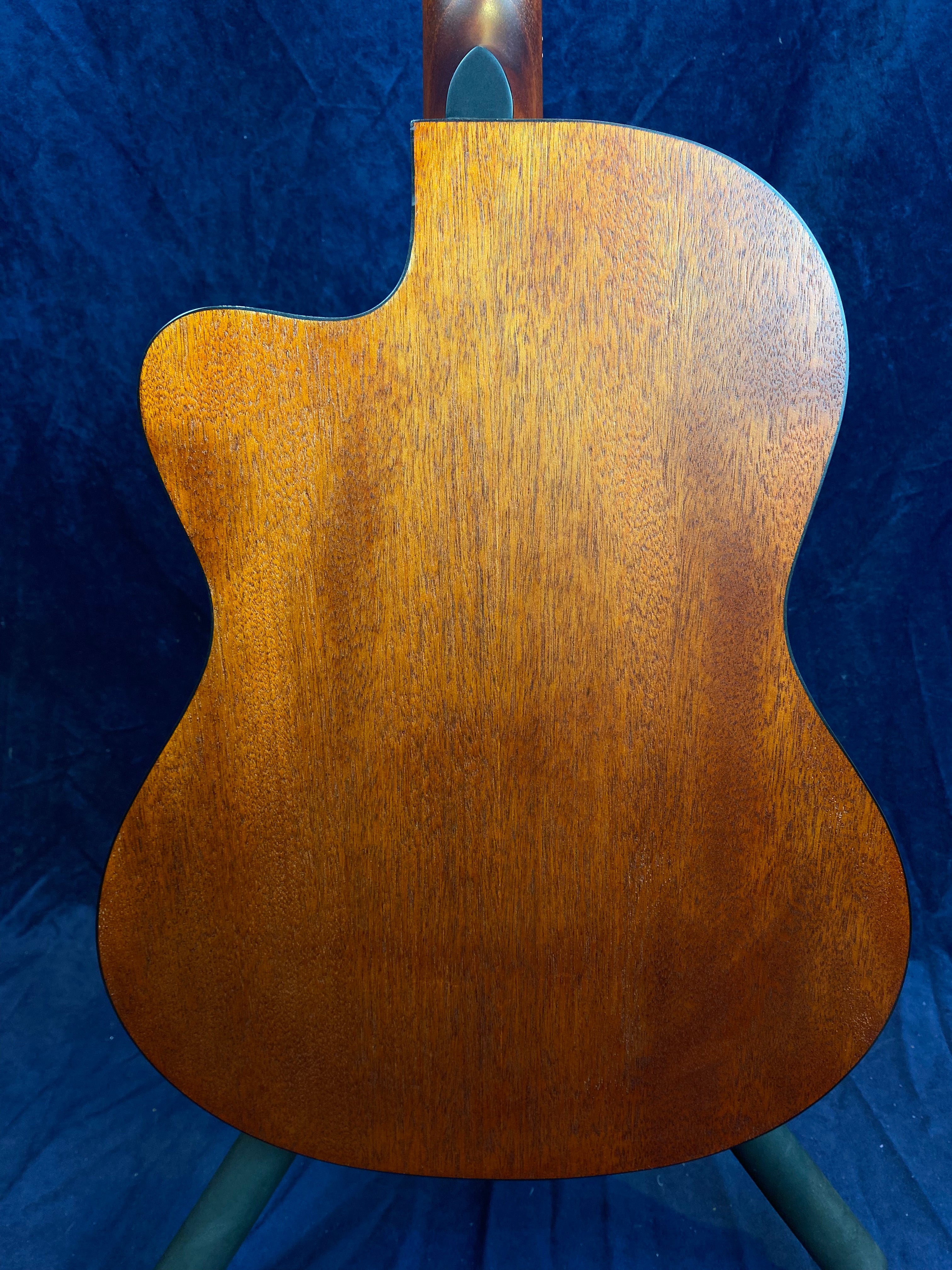 Mahogany acoustic guitar back with a smooth matte finish and a single cutaway for upper fret access, shown against a dark blue background.