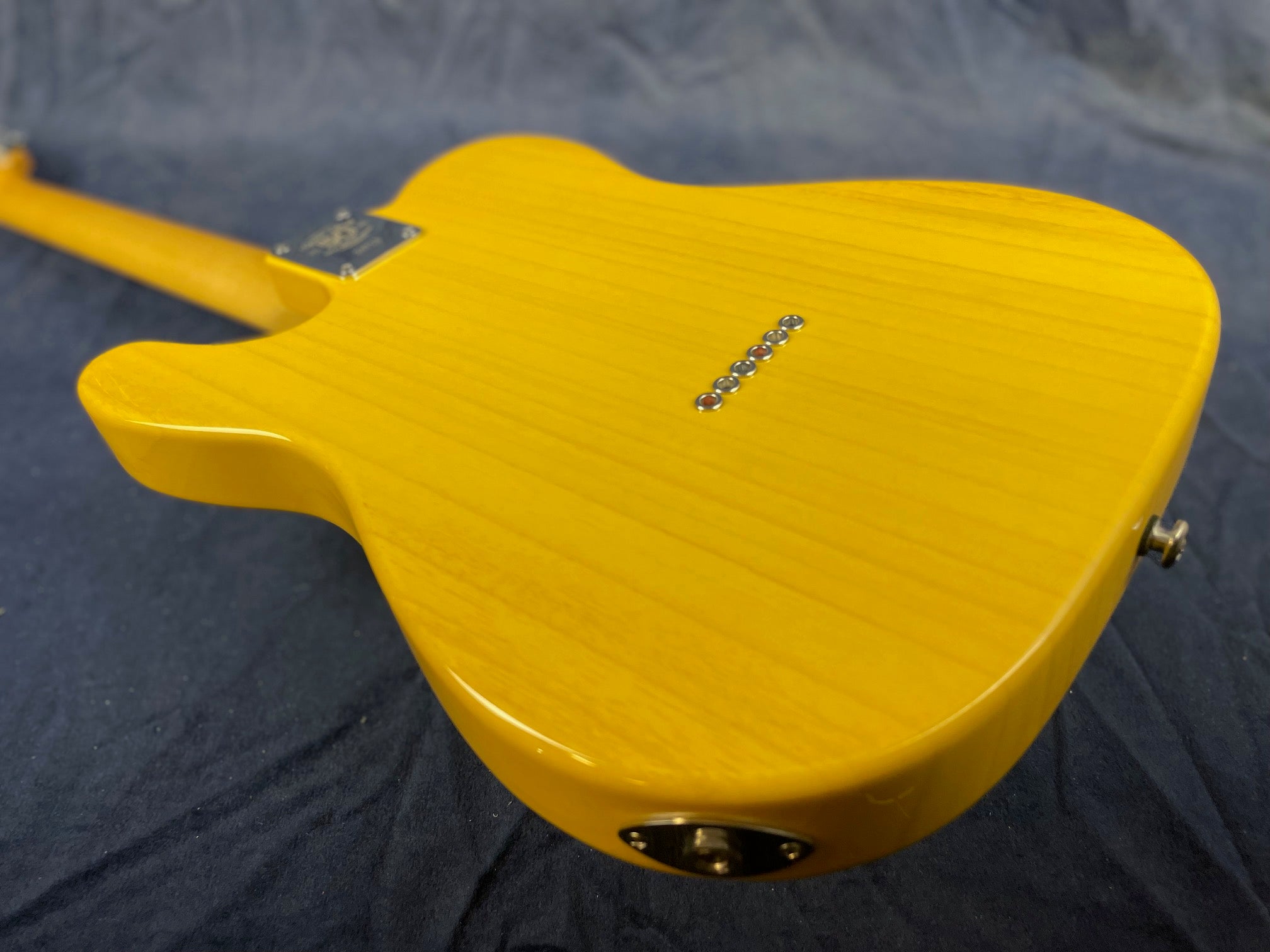 Yellow electric guitar body shown from the back with visible string ferrules and output jack, lying on a dark cloth surface.