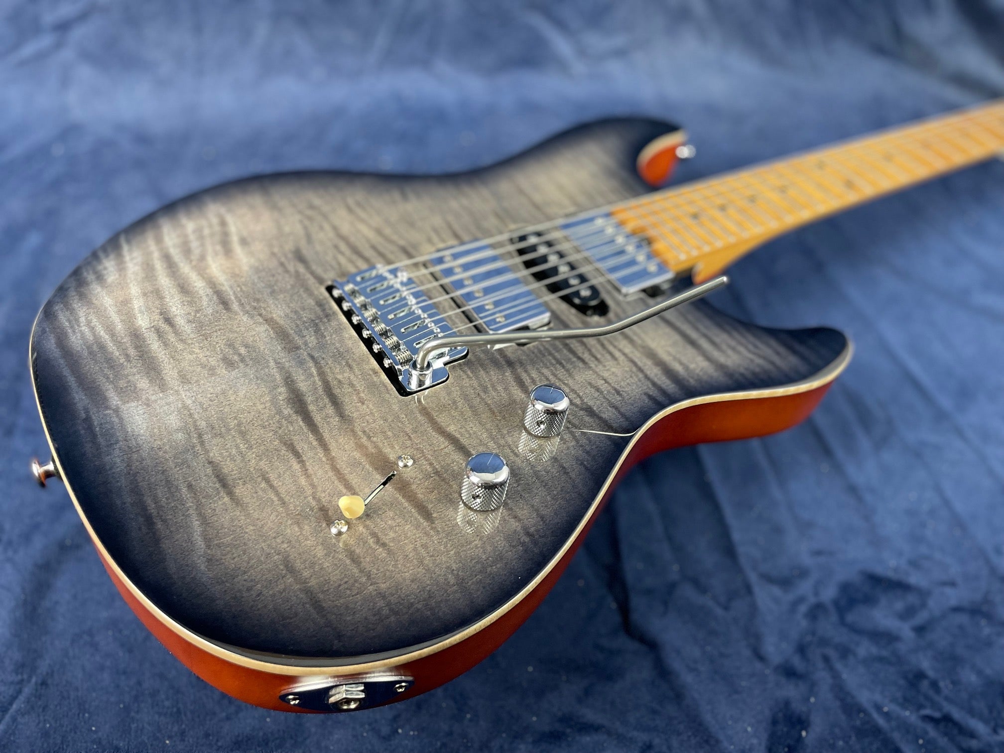 Electric guitar with a grey burst finish, two control knobs, a switch, a tremolo bridge, and a maple fretboard, body edges tinted amber.