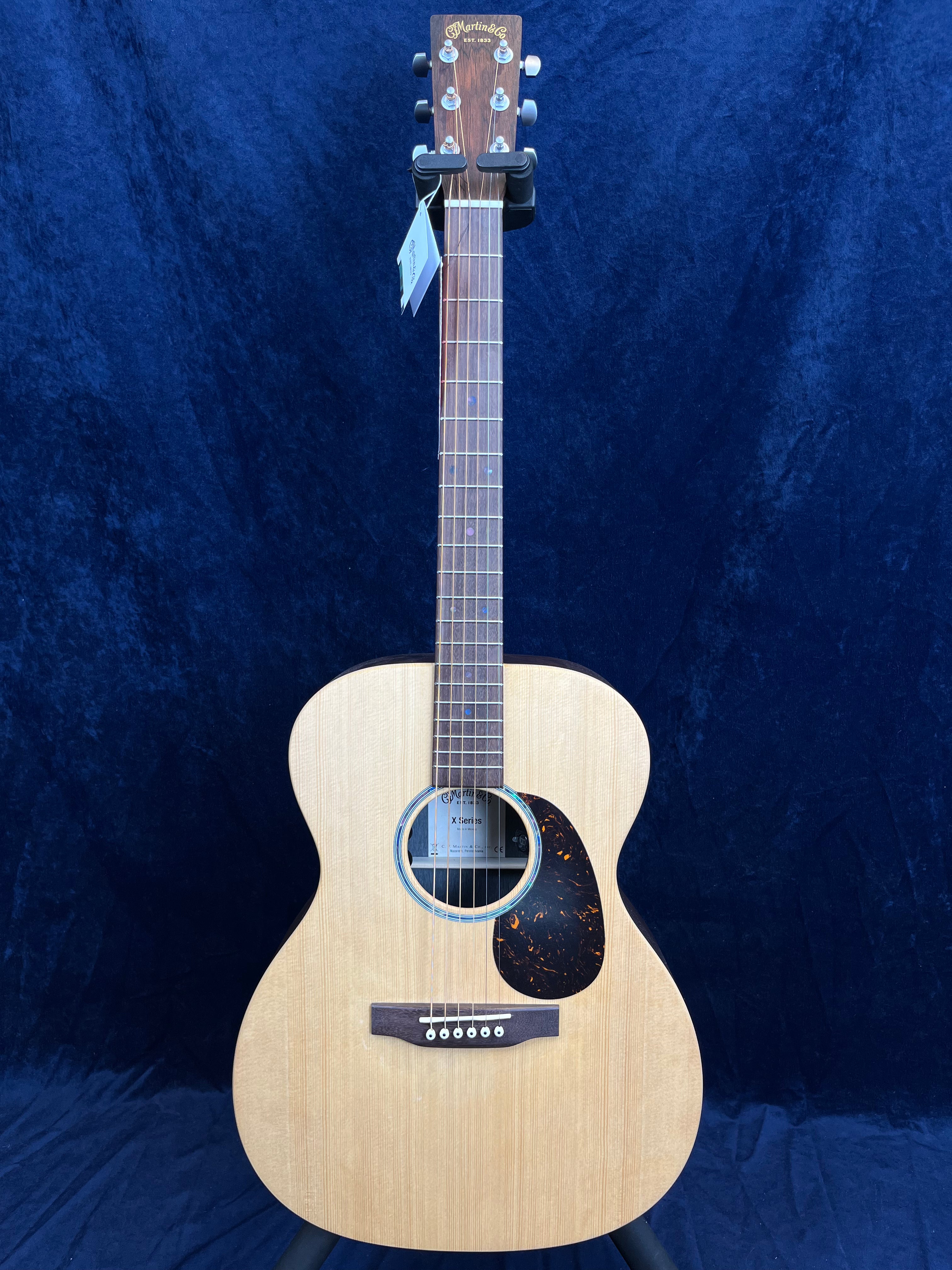 Light wood acoustic guitar with a rounded body, dark pickguard, six strings, and a Martin & Co. logo on the headstock, set against a dark blue background.