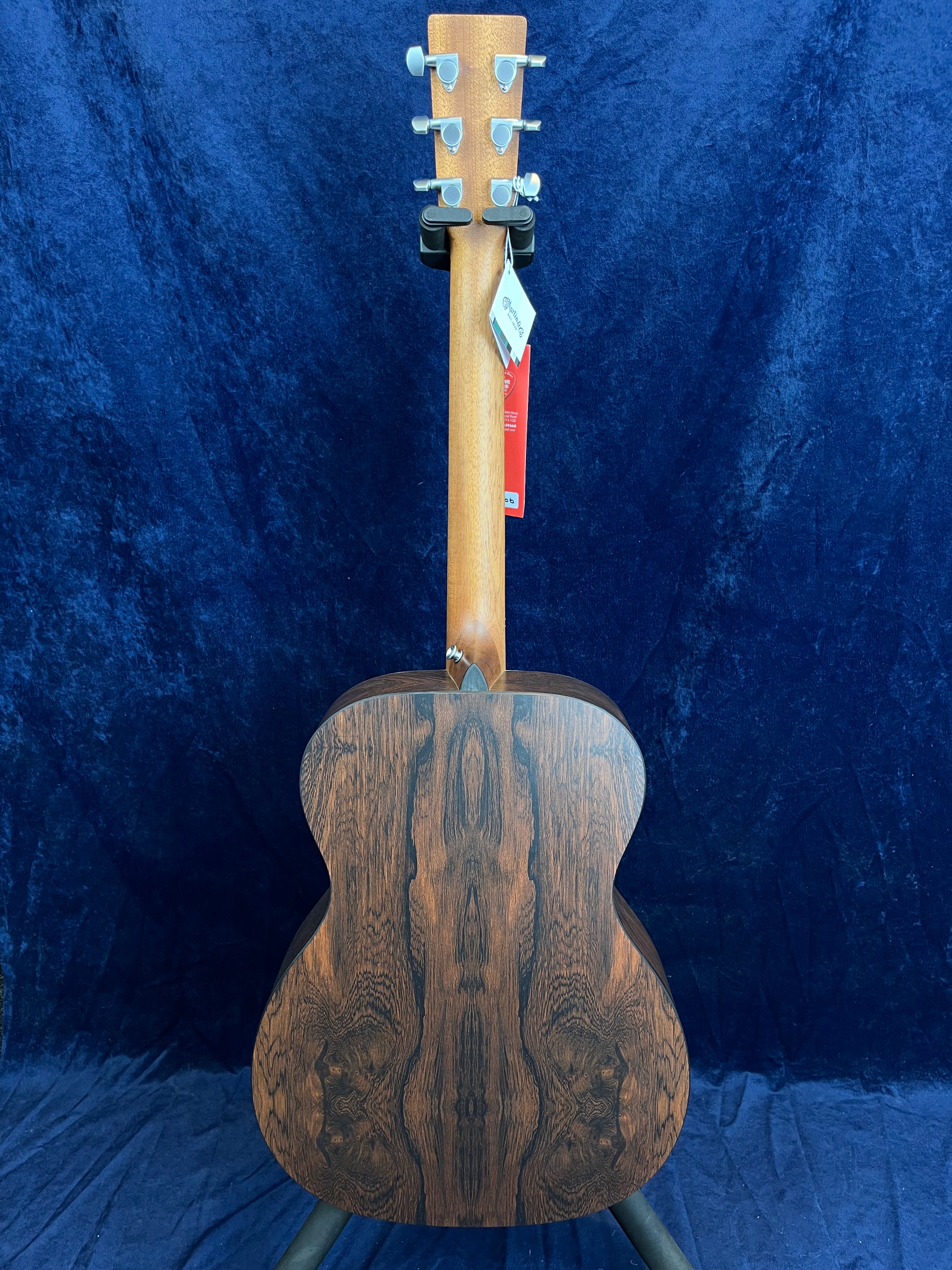 Acoustic guitar shown from the back, displaying dark, symmetrical wood grain patterns and silver tuning pegs against a deep blue background.