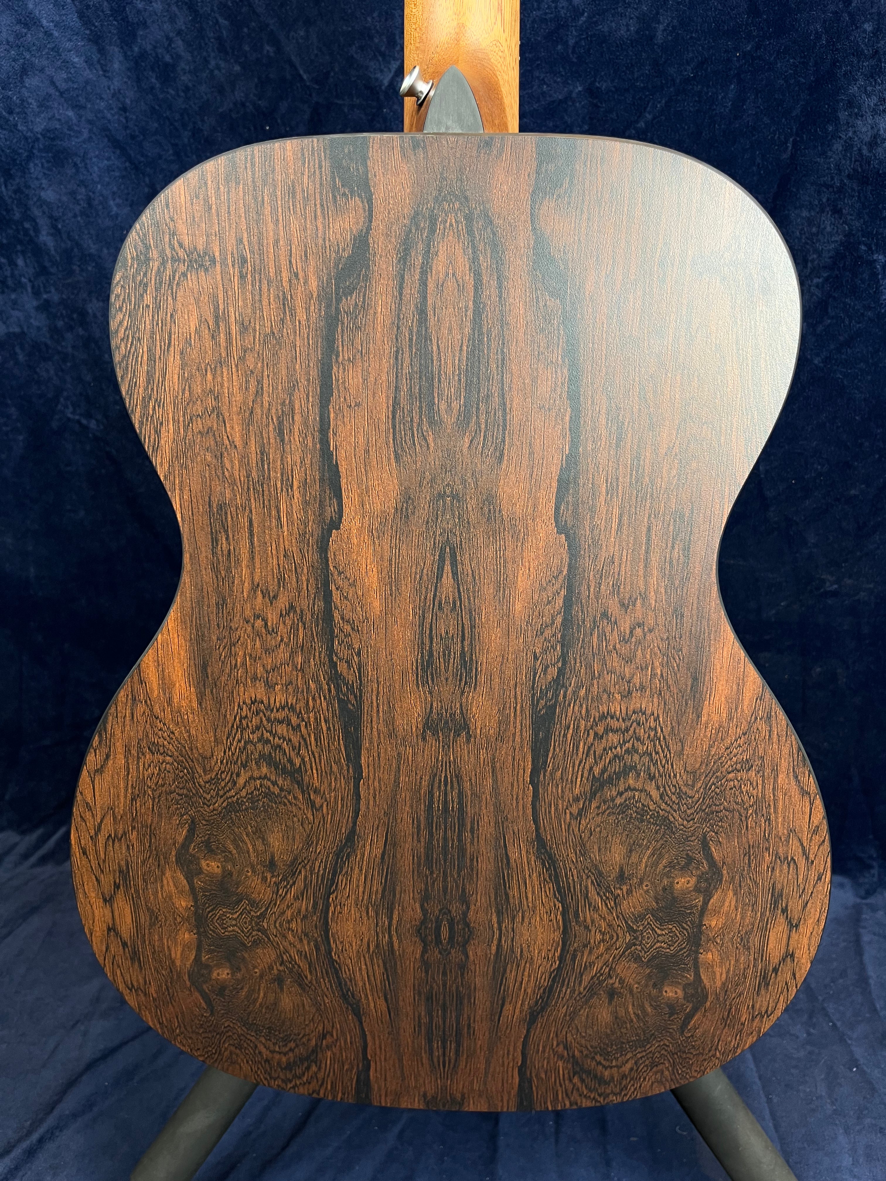 Back of an acoustic guitar with dark, symmetrical wood grain patterns and a smooth, glossy finish.