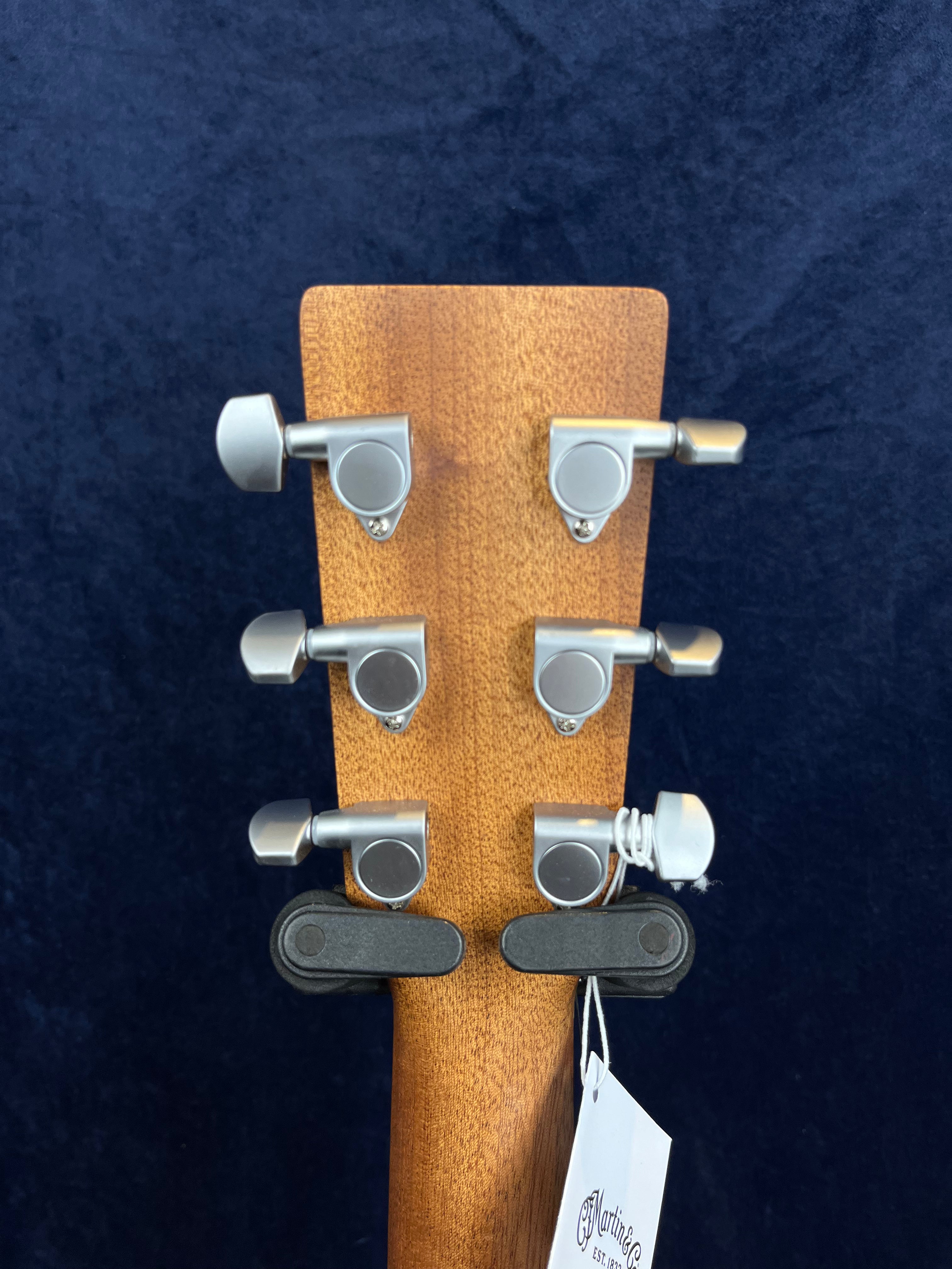 Six silver tuning pegs on the back of a wooden acoustic guitar headstock, with a string tied to one peg and a white tag hanging below.