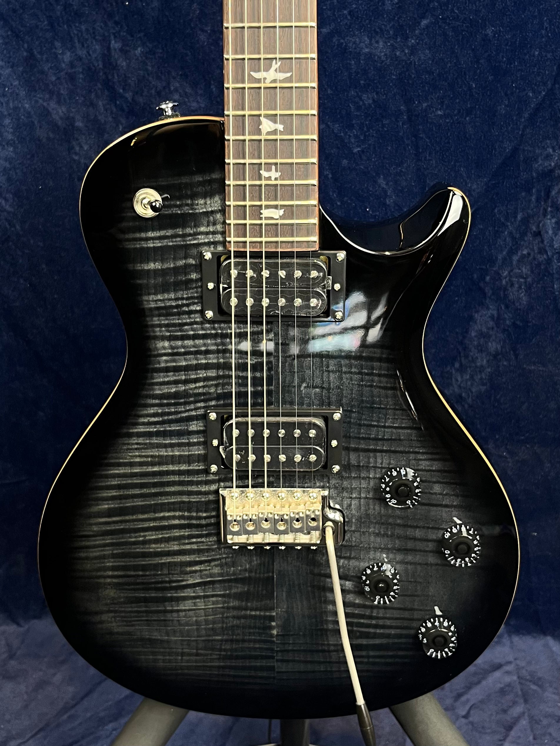 Glossy black electric guitar with a flamed maple top, two humbucker pickups, four control knobs, a whammy bar, and bird inlays on the fretboard.