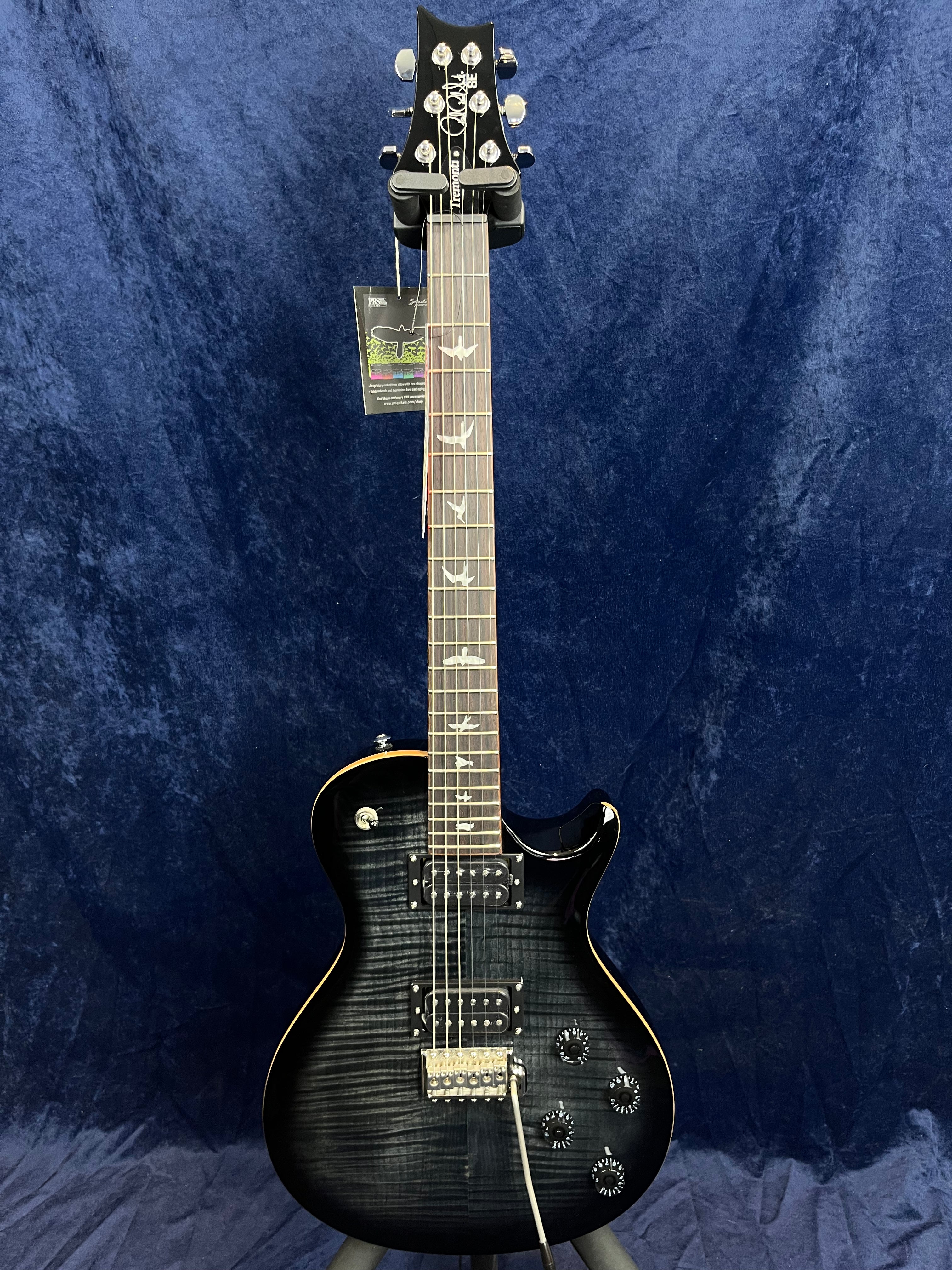 Black electric guitar with a glossy finish, two humbucker pickups, four control knobs, and bird-shaped inlays on the fretboard.
