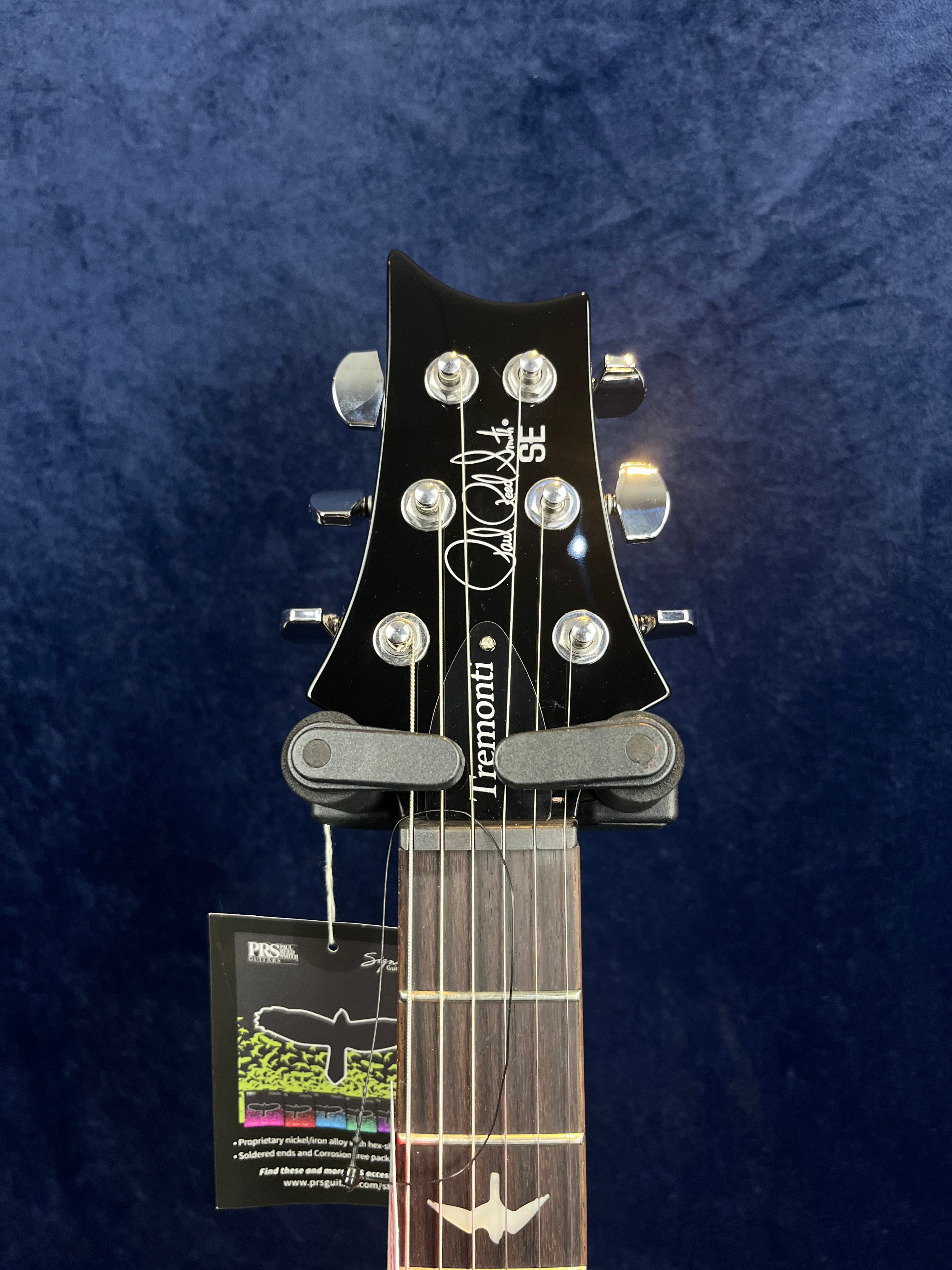 Black headstock of a PRS SE Tremonti electric guitar with six chrome tuning pegs and a bird inlay on the dark wood fretboard.
