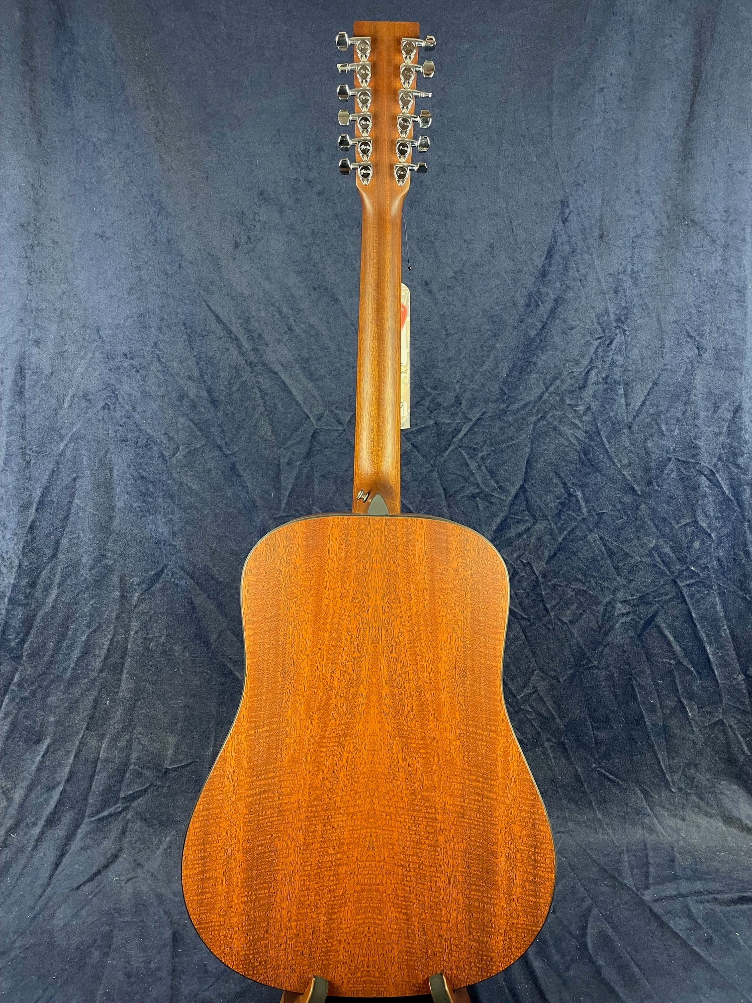 Twelve-string acoustic guitar viewed from the back, showing a polished brown wood body and neck with six pairs of chrome tuning pegs.