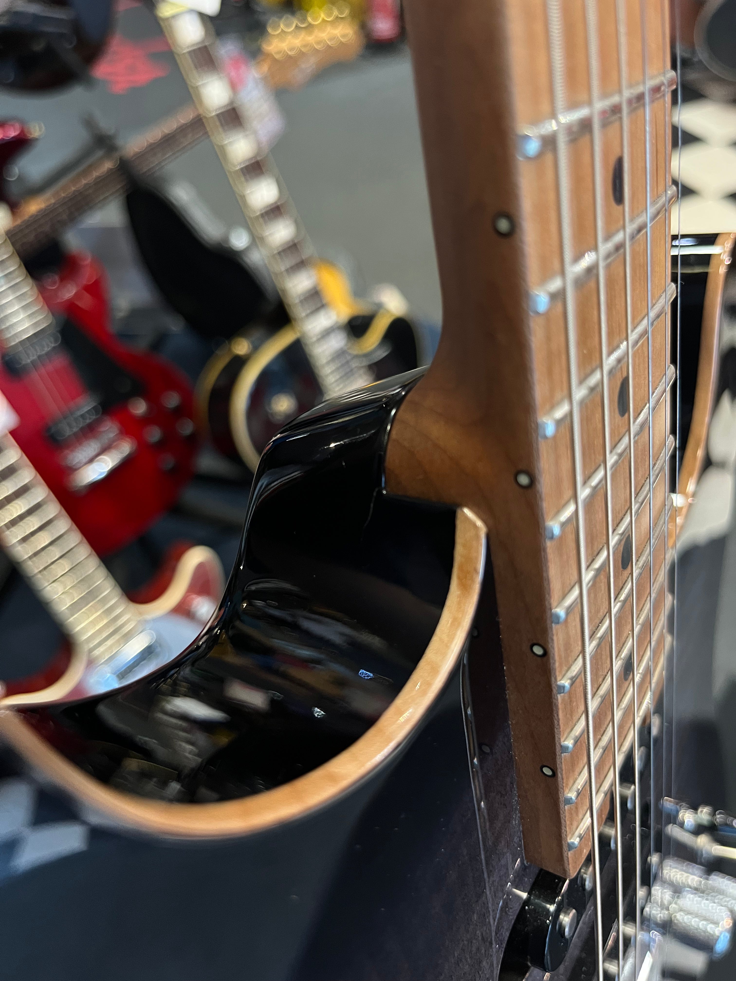 Close-up of an electric guitar's neck joint and fretboard, with other guitars blurred in the background on a display stand.