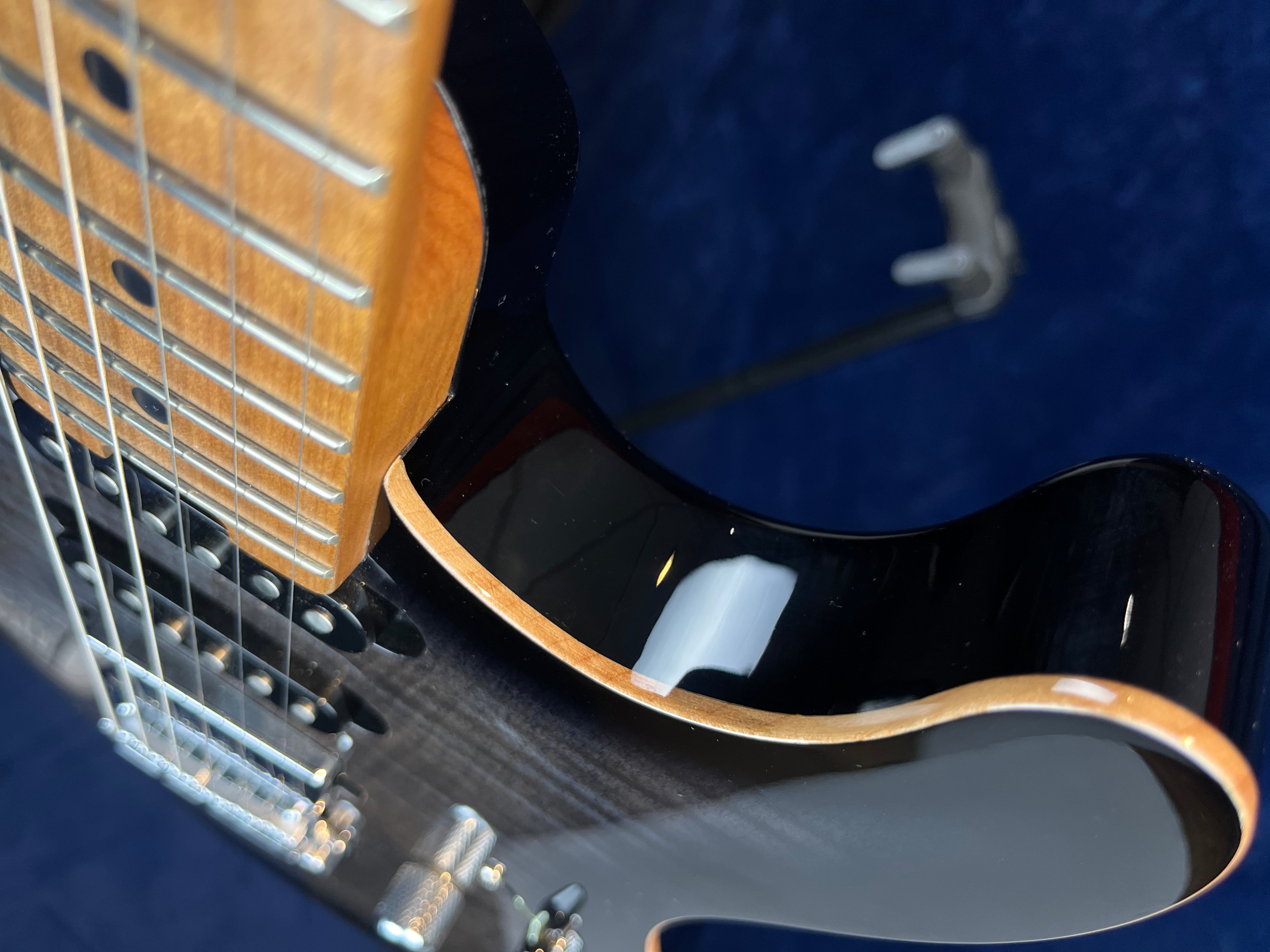 Close-up of a glossy black electric guitar showing part of the neck, strings, pickups, and smooth contoured body with a natural wood edge.