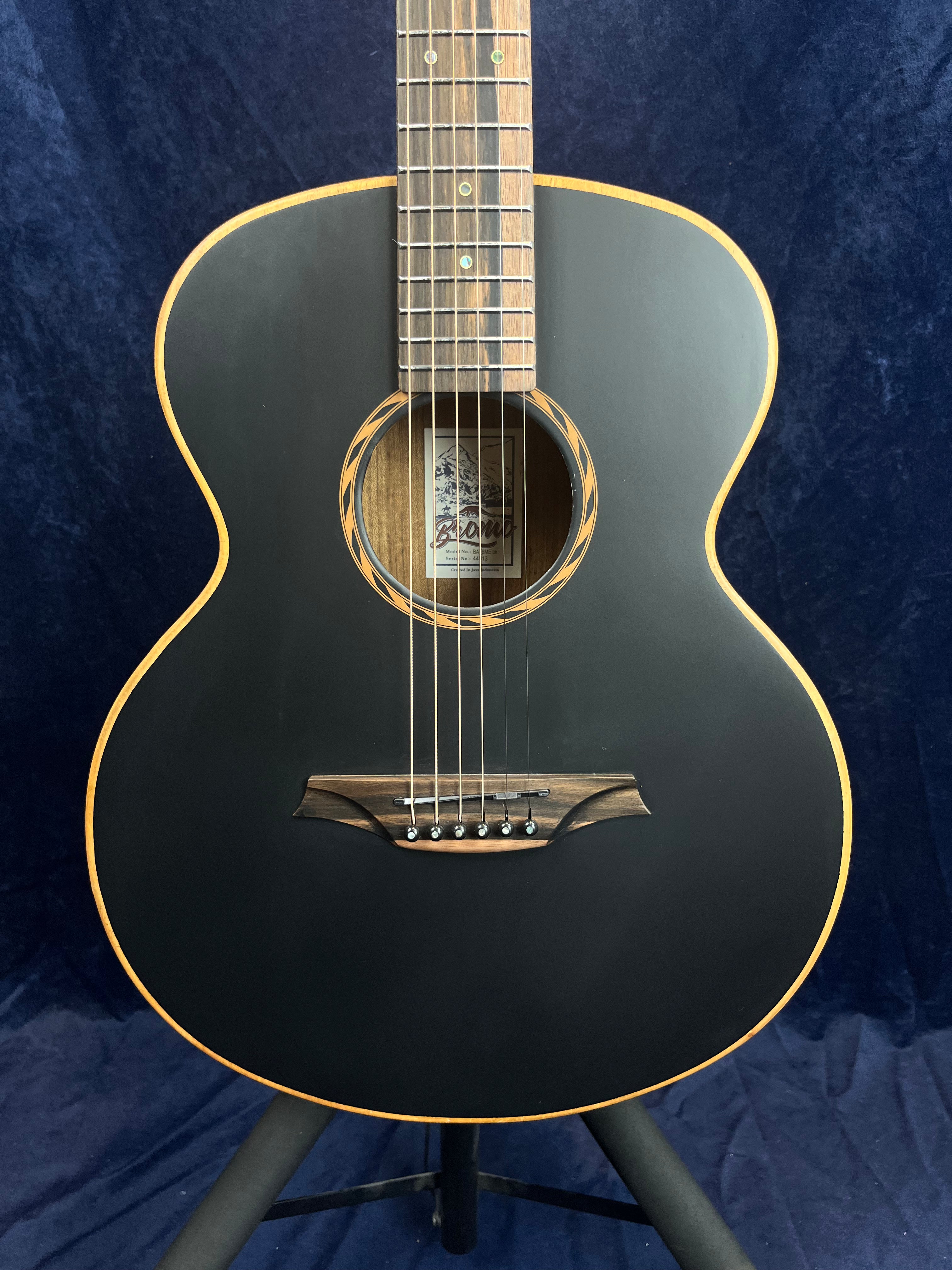 Guitare acoustique à finition noire mate, contours bois clair, rosace décorative, chevalet et touche en bois foncé, six cordes.