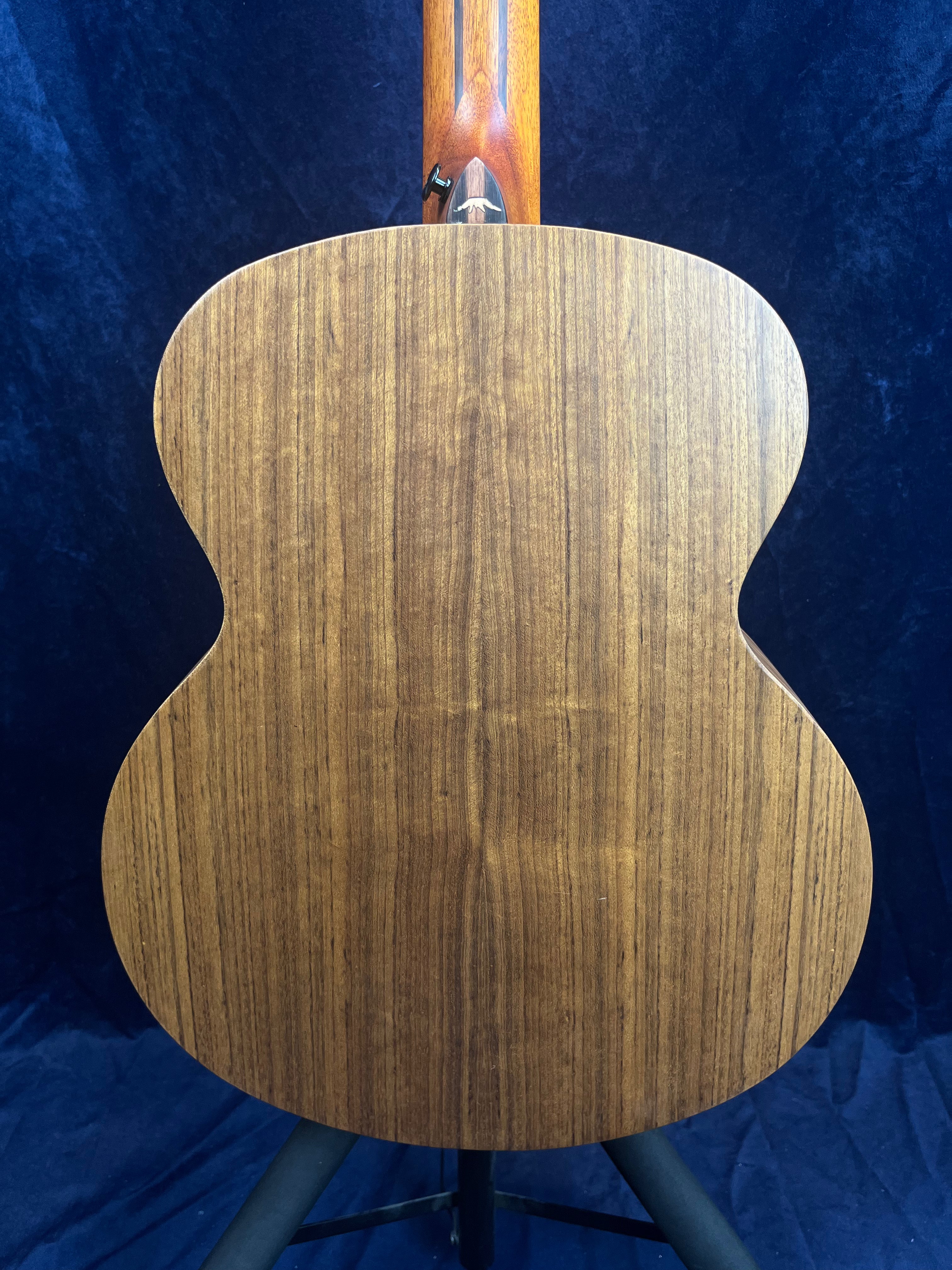 The back of an acoustic guitar with smooth, brown wood grain and a natural finish, shown against a dark blue background.