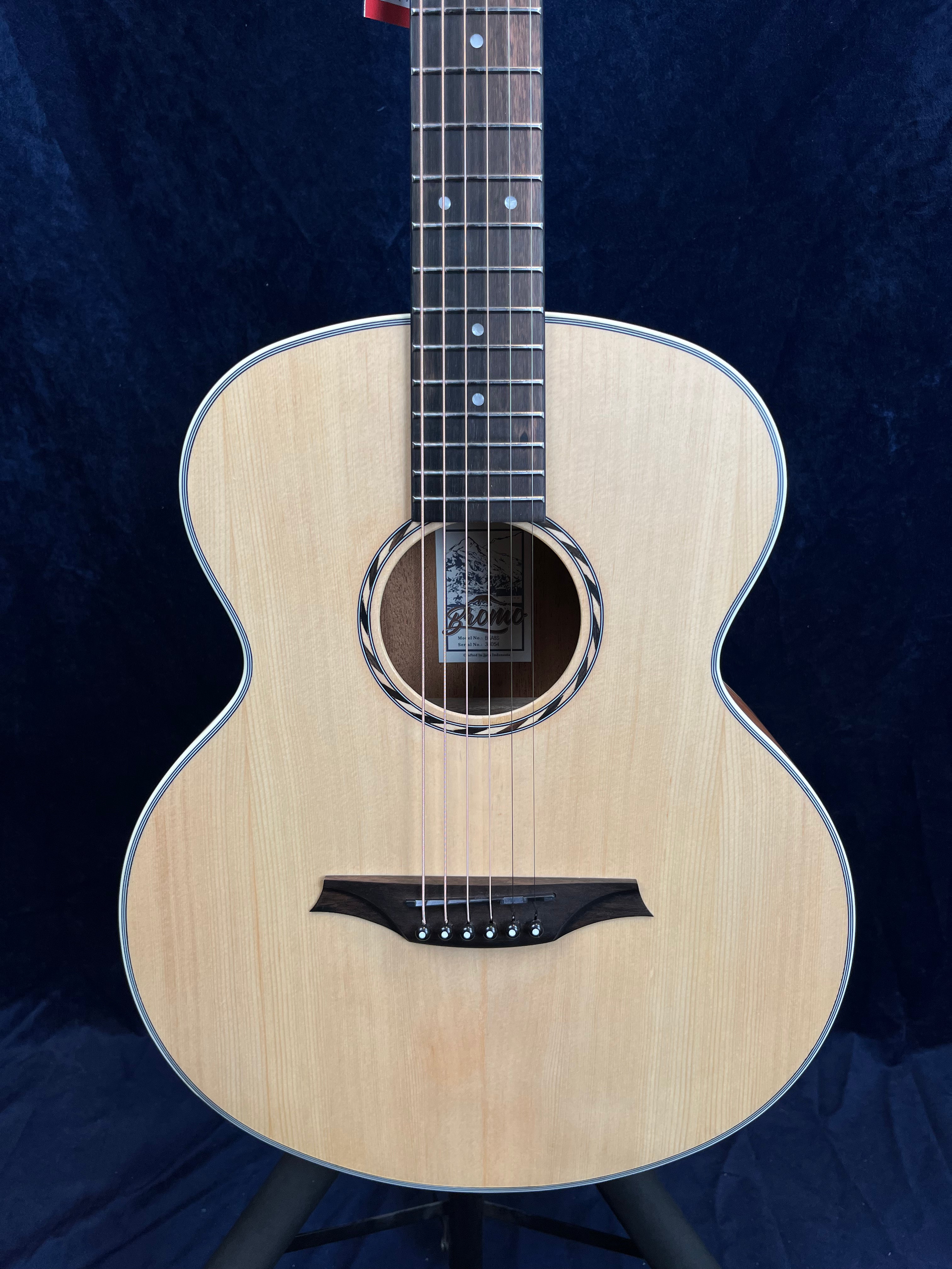 Light wood acoustic guitar with a dark wooden bridge, round soundhole, and steel strings against a dark background.