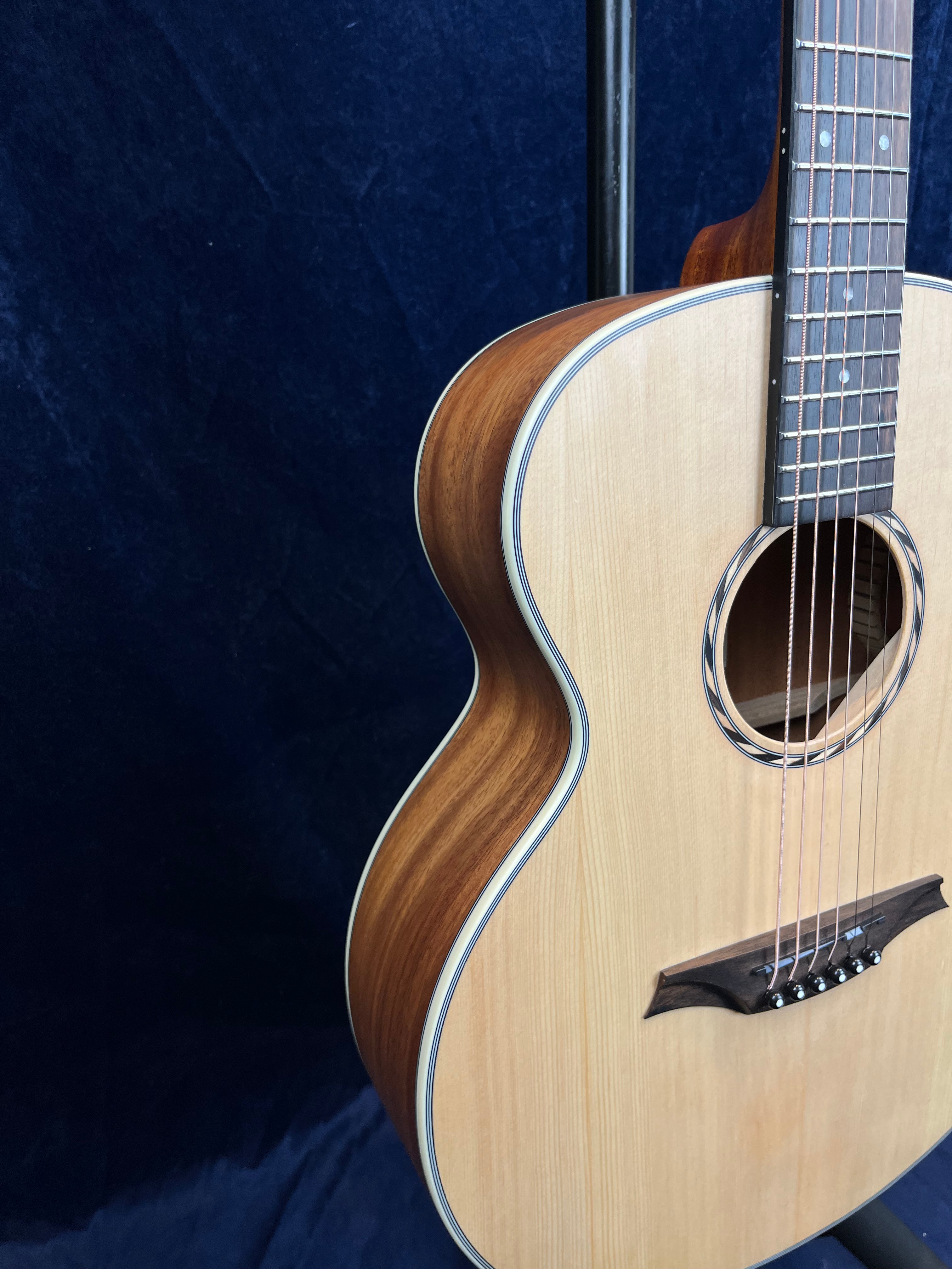 Light wood acoustic guitar with a dark wood bridge and sides, shown on a dark blue background. Only the lower half and part of the neck are visible.