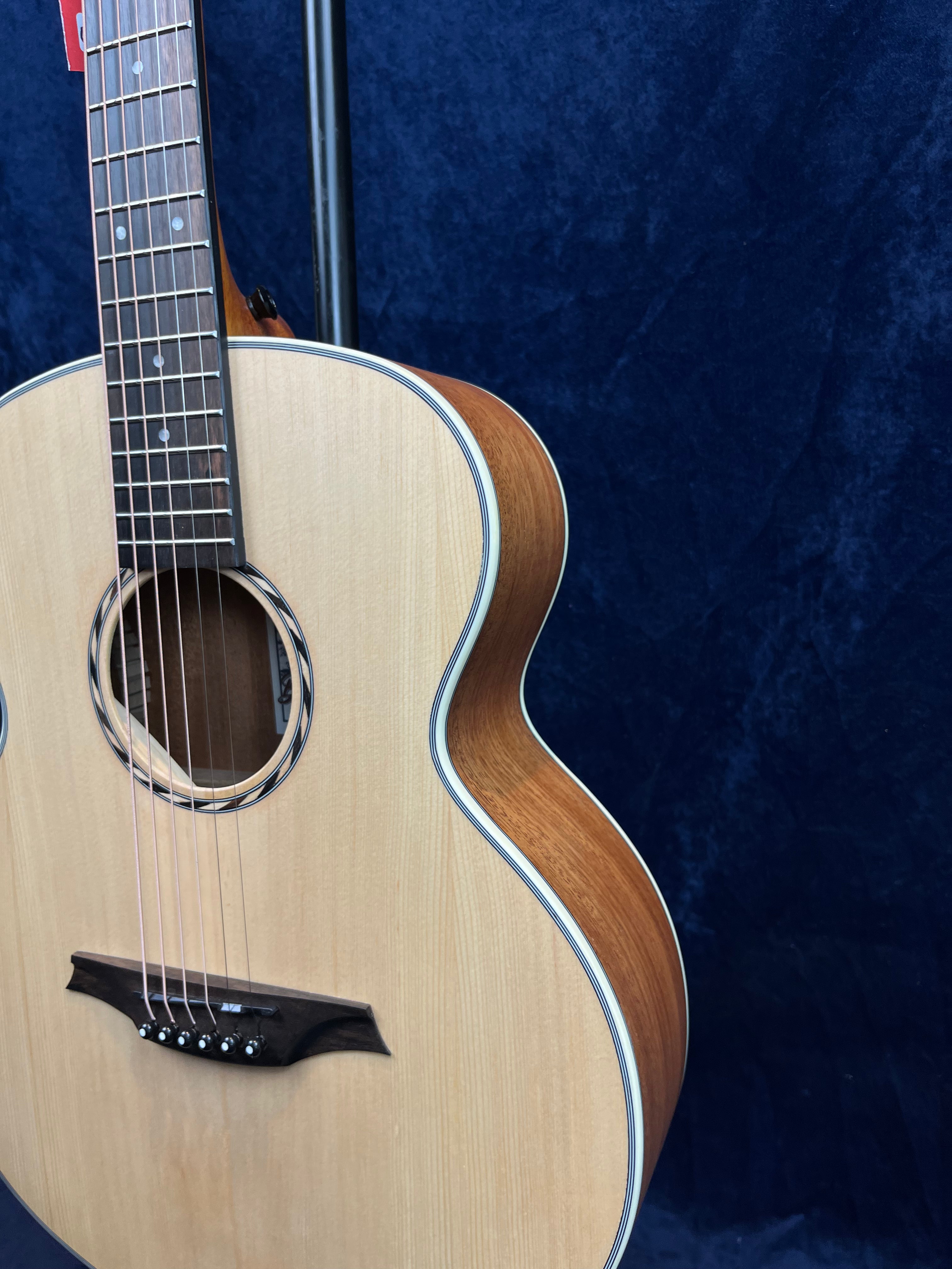 Light wood acoustic guitar with a dark wood bridge and sides, white trim around the body, and dot inlays on the fingerboard, set against a dark blue background.