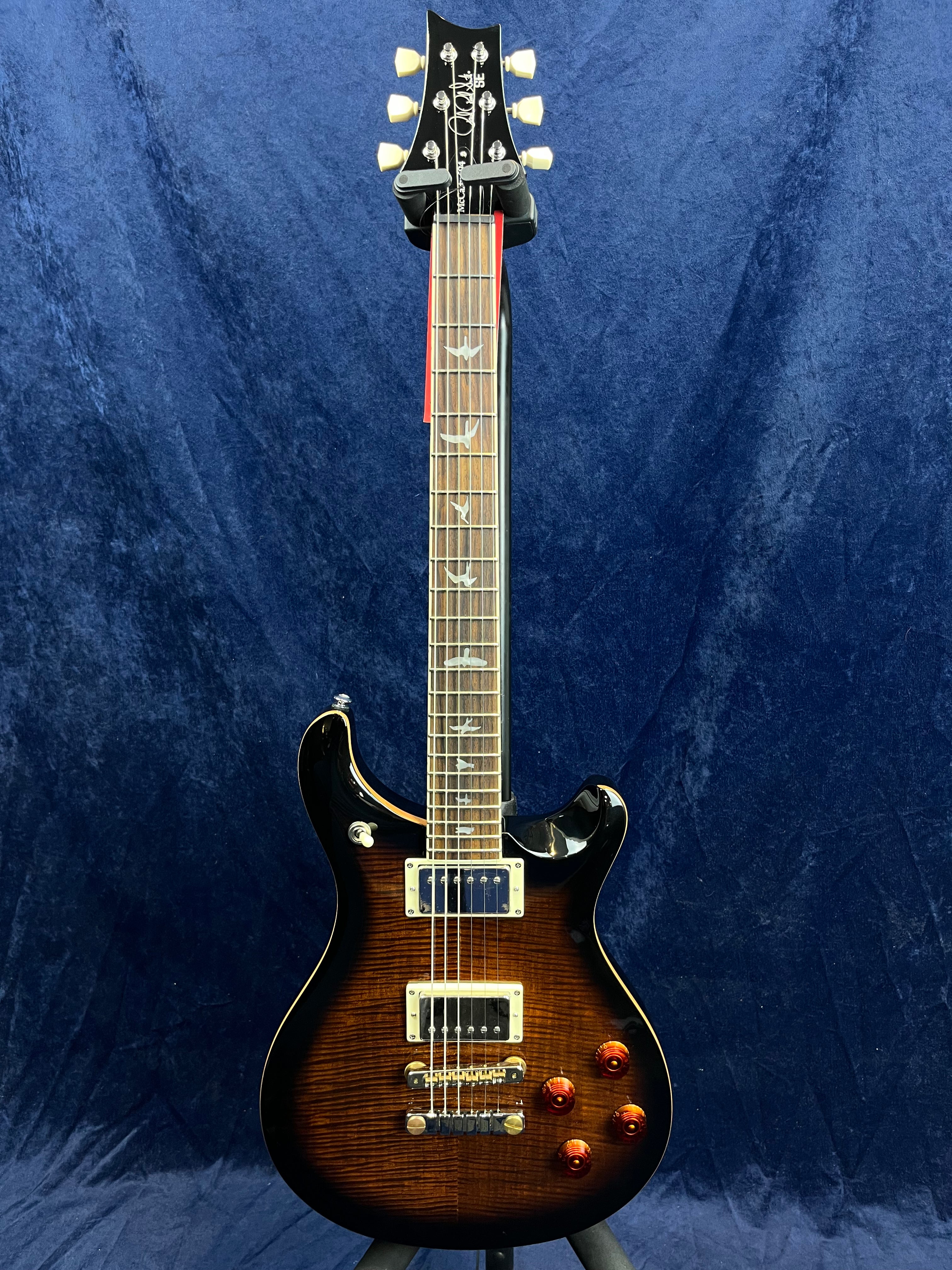 Electric guitar with a dark sunburst finish, two humbucker pickups, four amber control knobs, and bird-shaped inlays along the fretboard.
